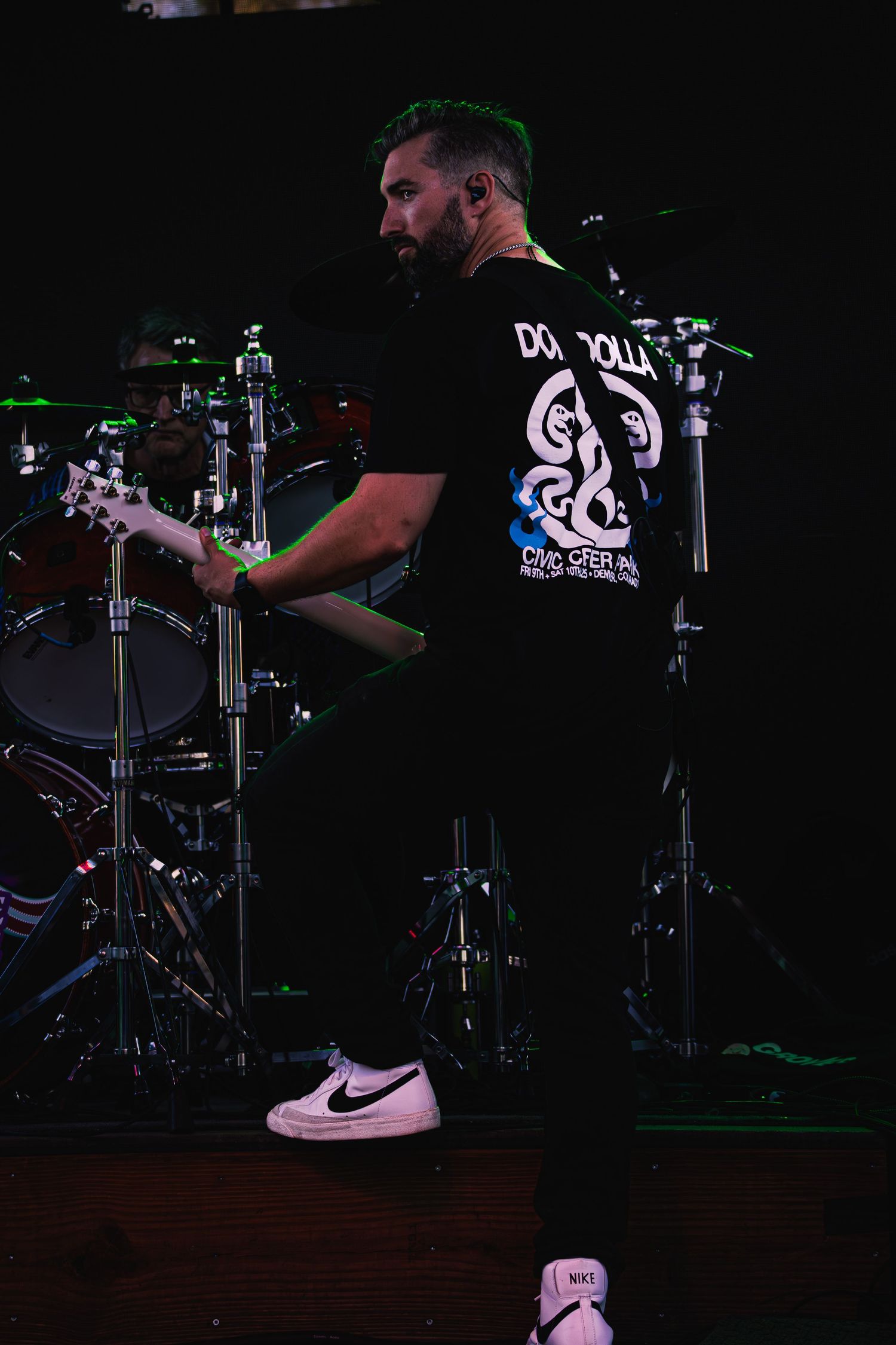 Guitarist playing next to the drum set looking over his shoulder during performance