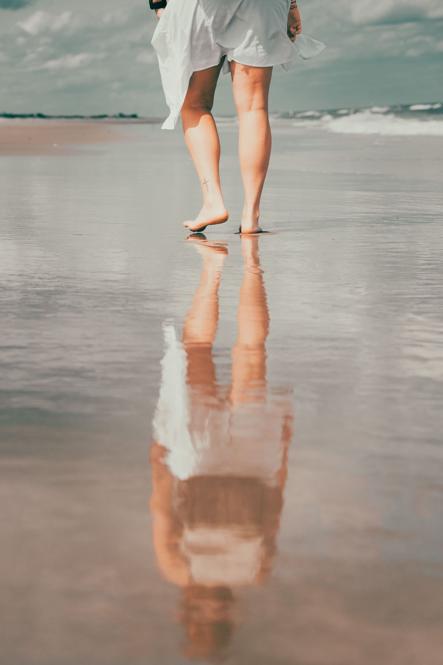 Reflection of a girl walking along the beach on the sand