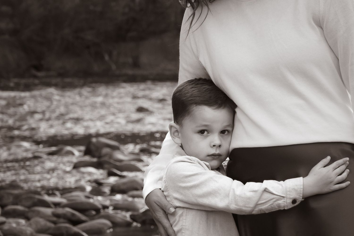 Black and white photo of child hugging his mother by the river