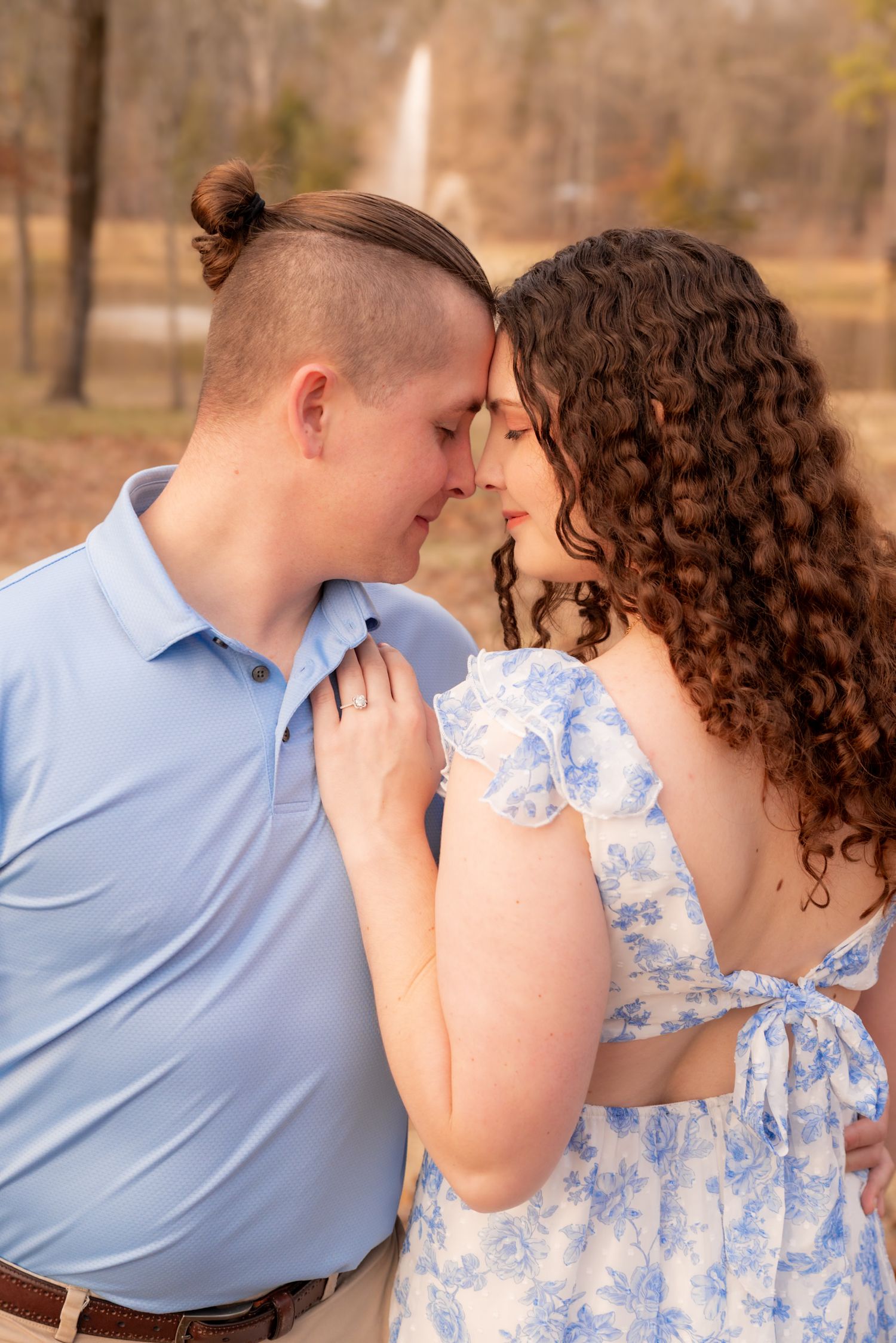 Couple in blue outfits sharing a romantic forehead touch outdoors during golden hour.