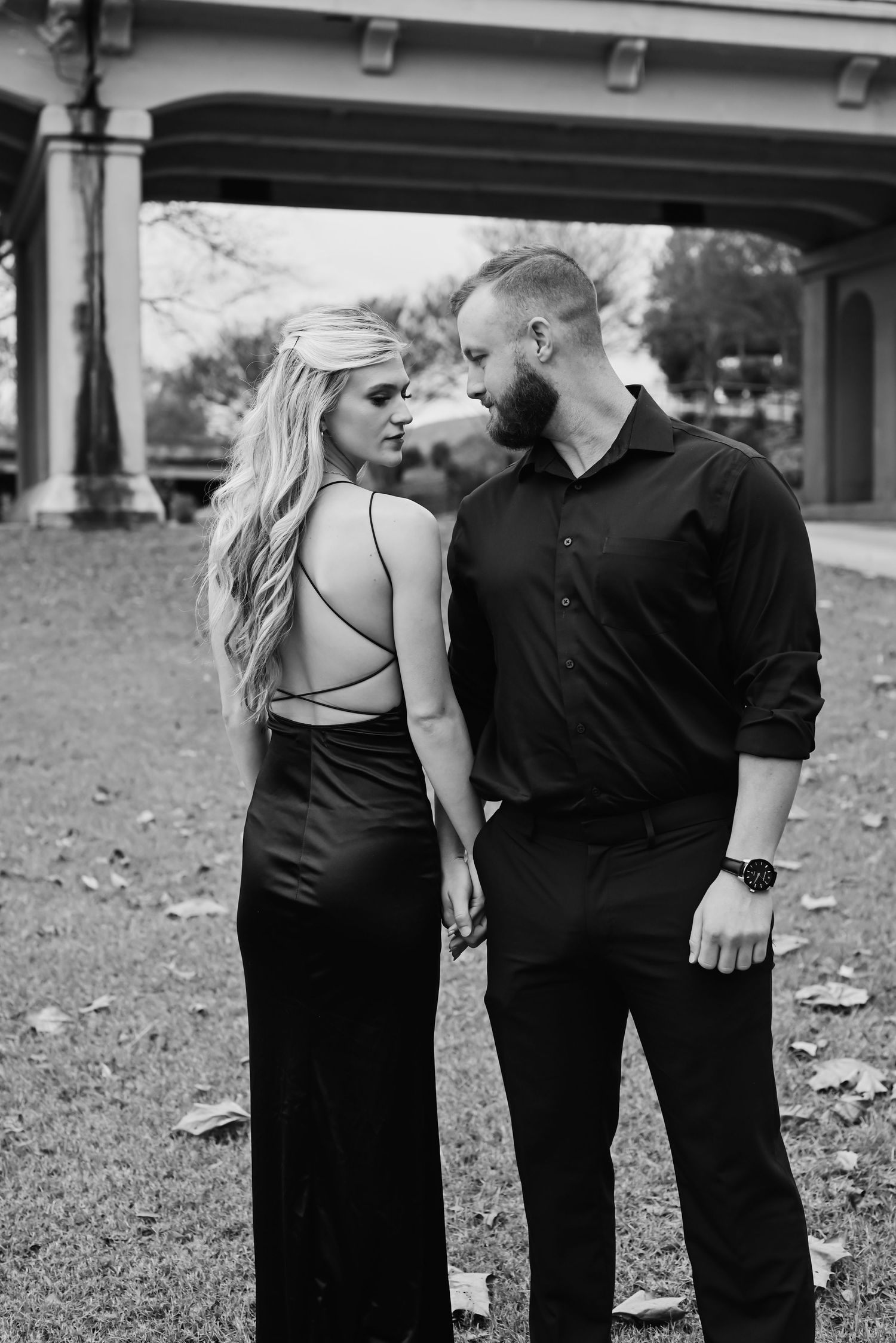 Stylish couple in black outfits sharing a close moment in a black and white outdoor photo.