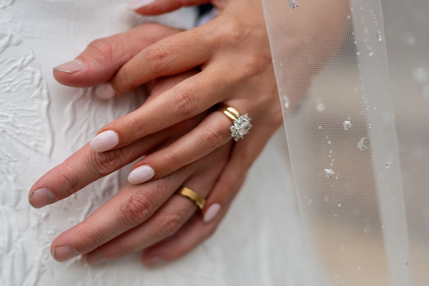 Close-up of mississippi bride and groom hands showing gold wedding bands and diamond engagement ring on white lace dress.
