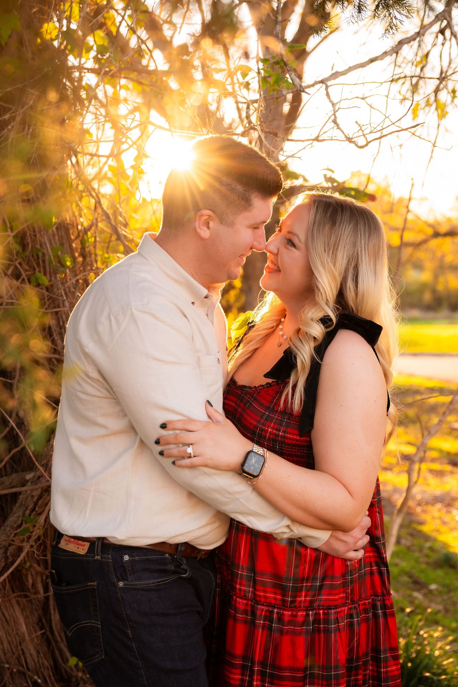 Couple sharing a romantic almost-kiss bathed in golden sunset light beneath a leafy tree.