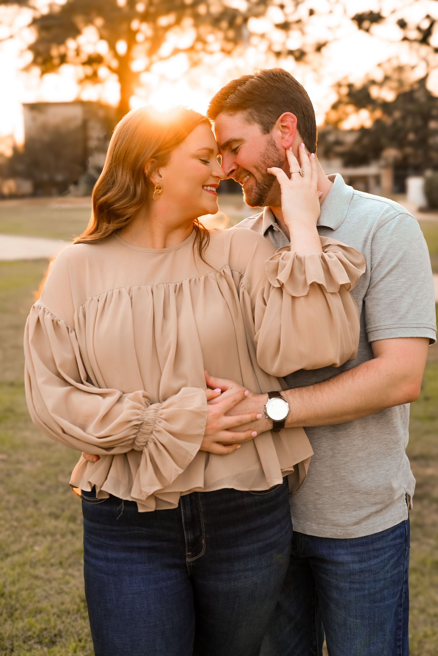Happy couple embracing at sunset in a park, woman in beige ruffled top and man in gray shirt.
