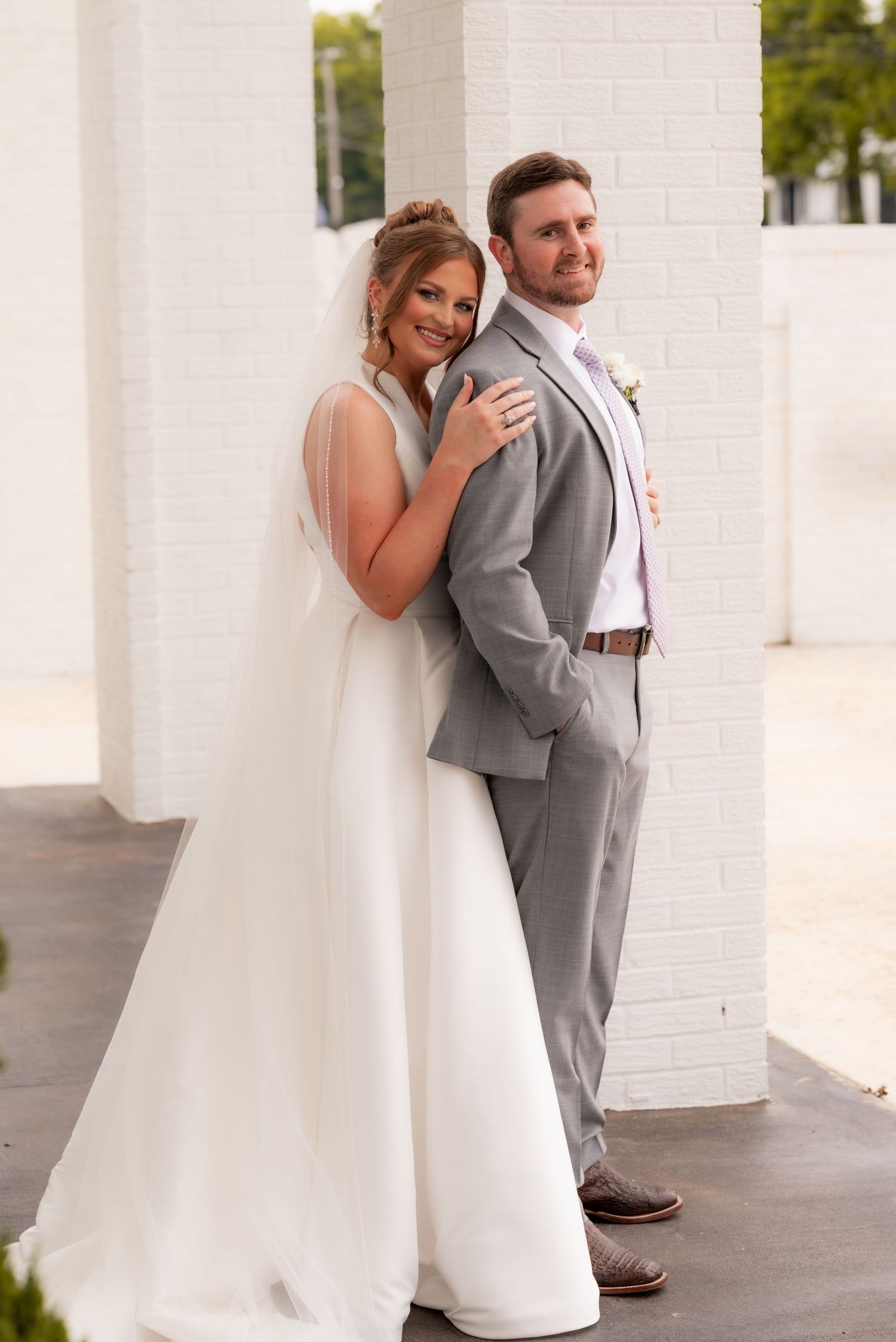 Bride and groom posing back-to-back between white brick columns in elegant wedding portrait.