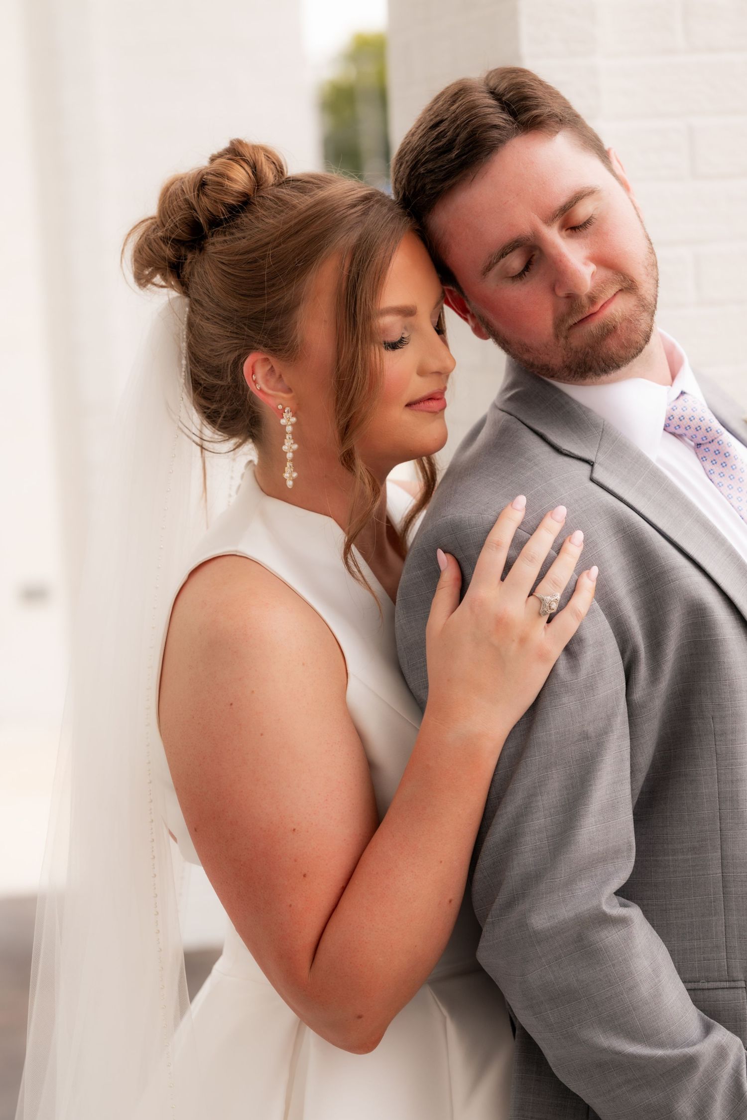 Bride and groom sharing intimate moment, bride in white gown with veil, groom in gray suit.