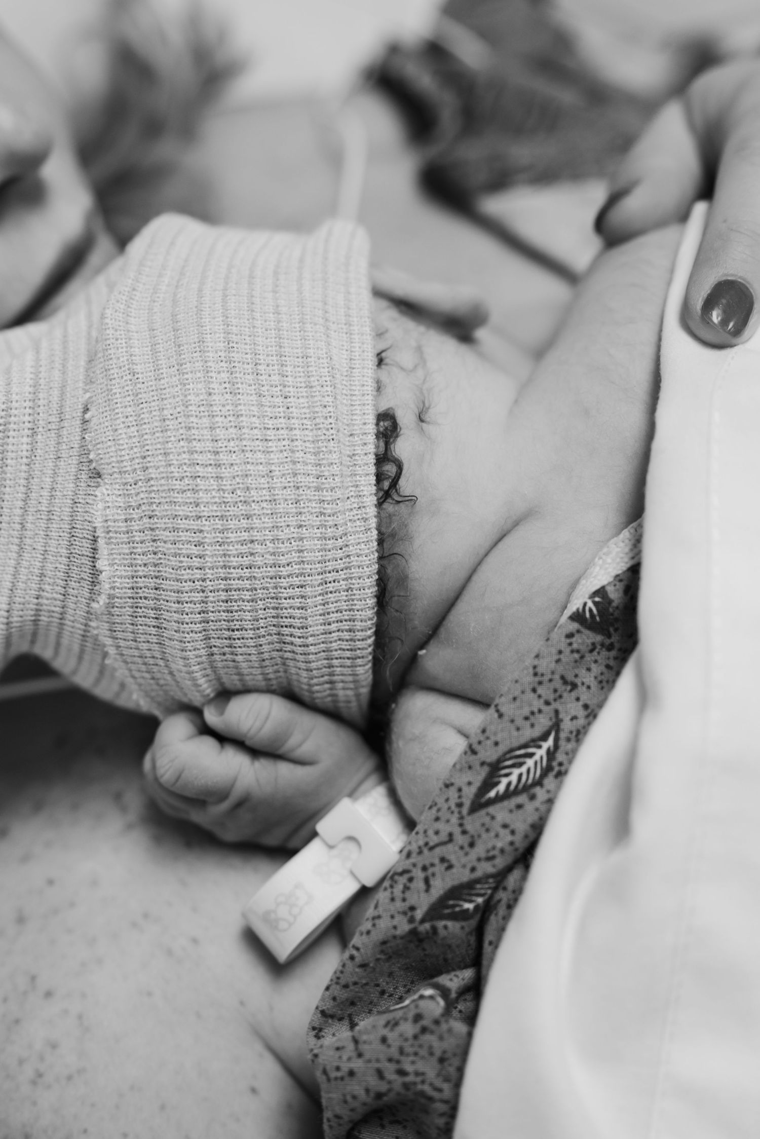 Black and white close-up of newborn baby holding adult finger with hospital ID bracelet.