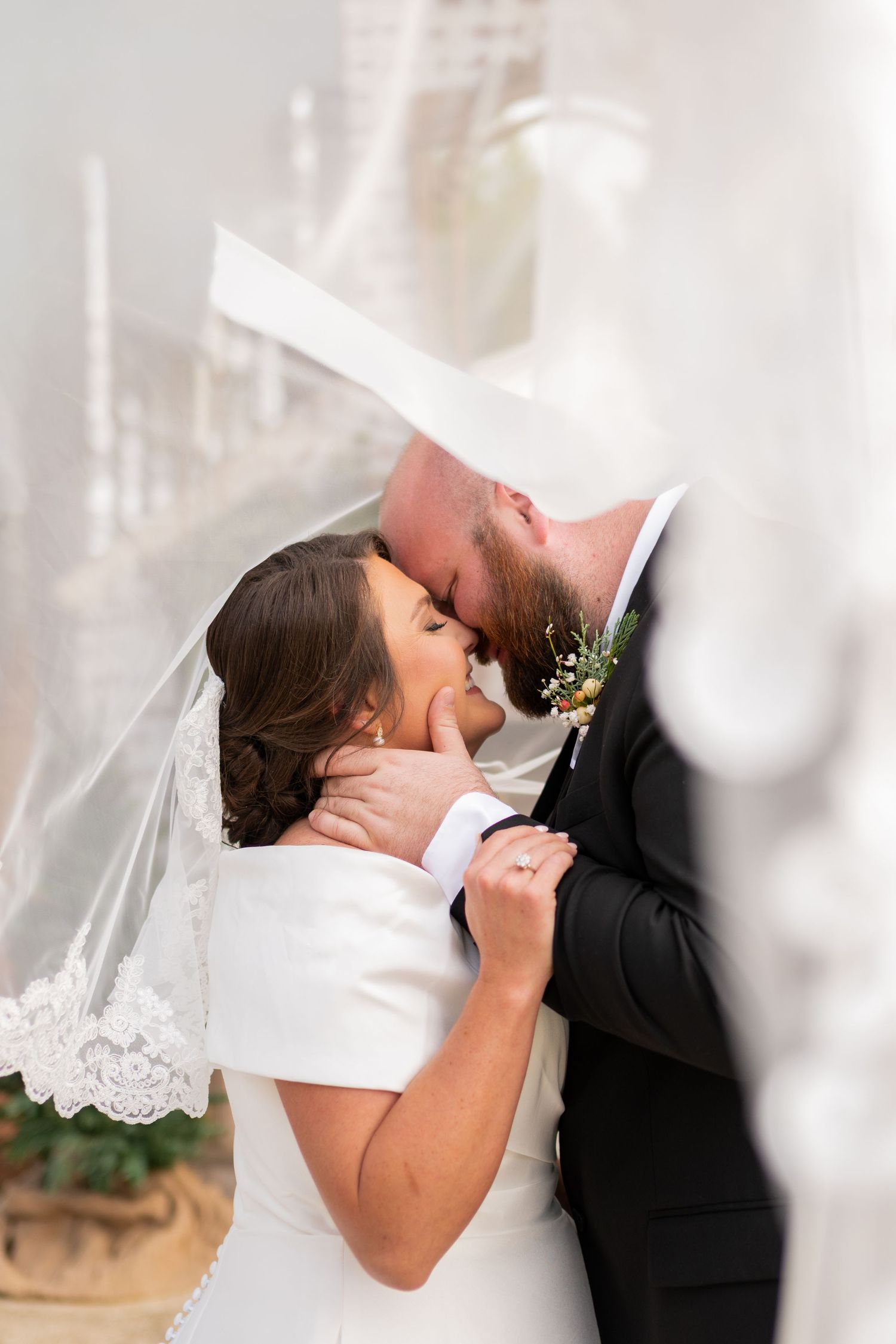 Bride and groom sharing romantic kiss under flowing white veil at wedding ceremony.