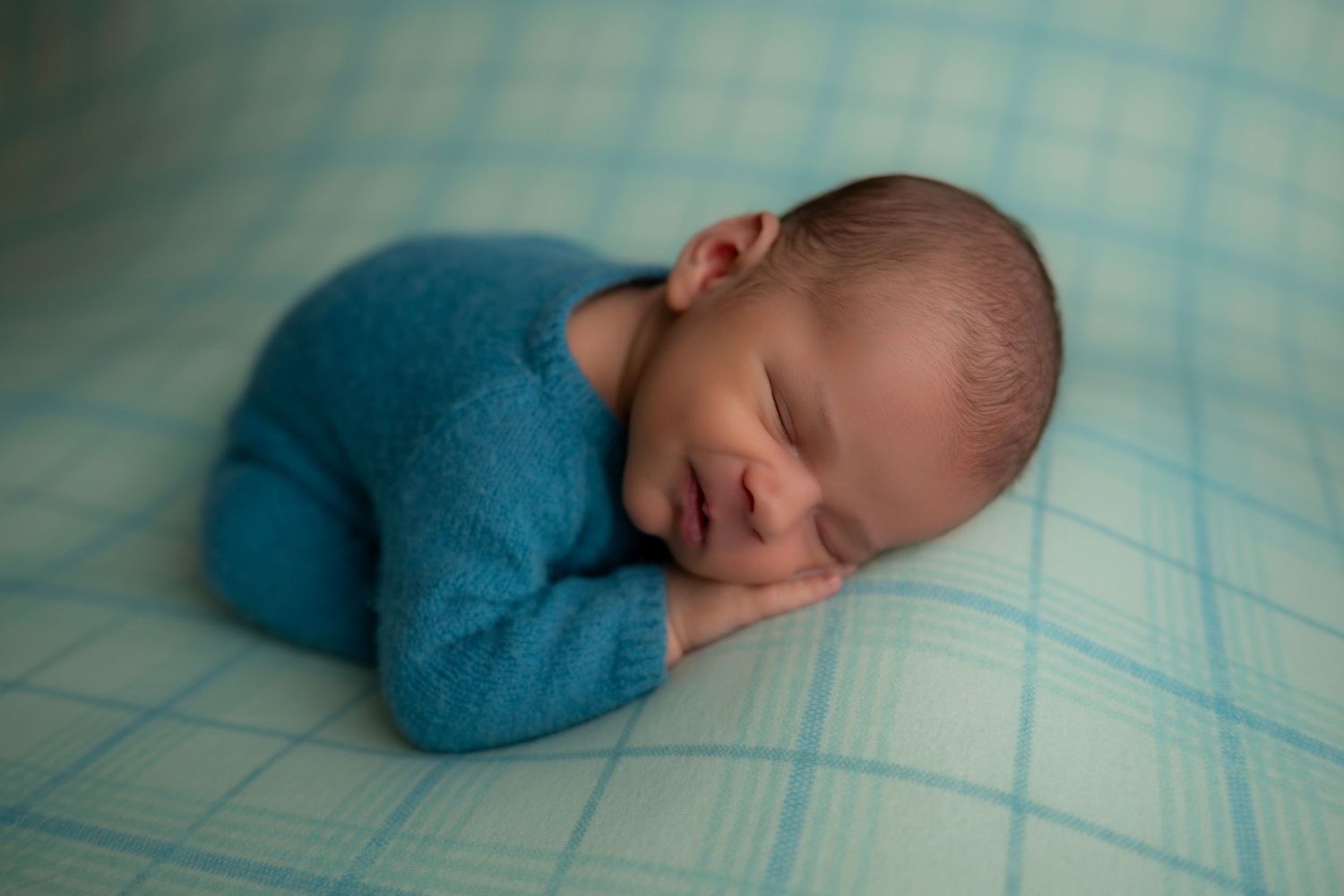 Newborn baby sleeping peacefully in teal knit wrap on blue blanket.