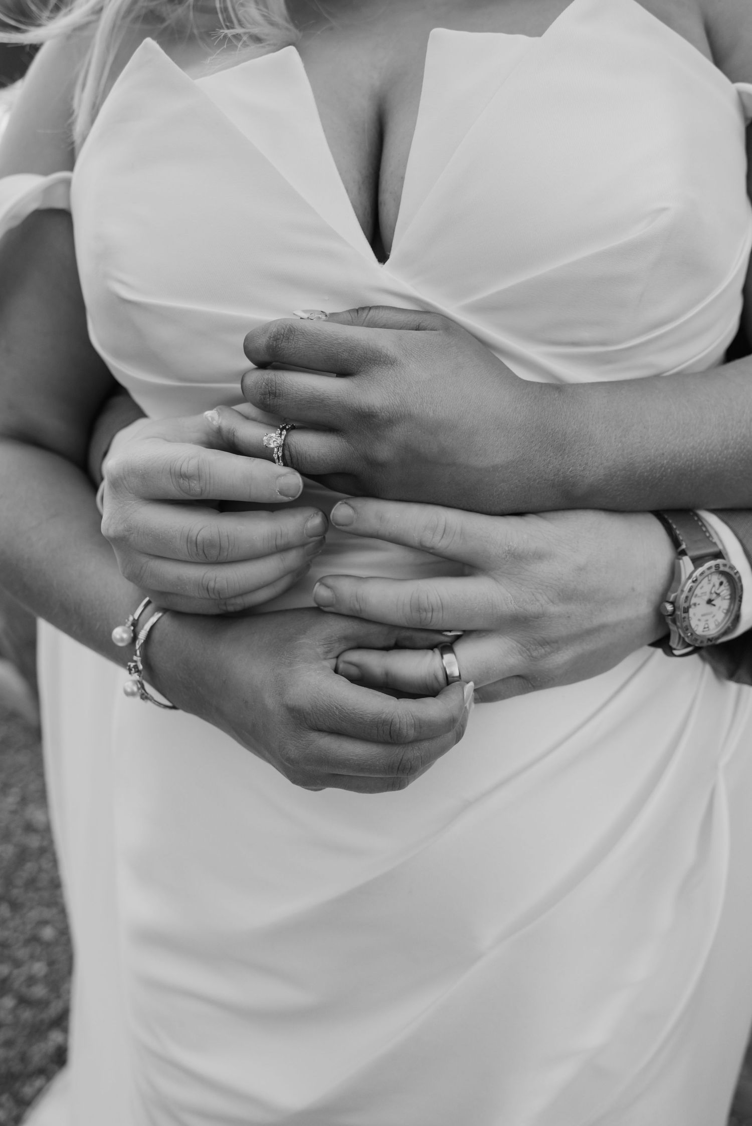 Black and white close-up of couple embracing, showing wedding rings and watches during romantic wedding moment.