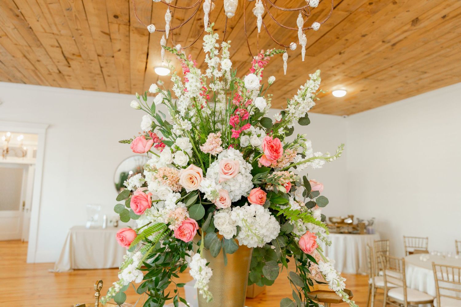 Elegant tall floral arrangement with pink and white roses in gold vase at wedding reception.