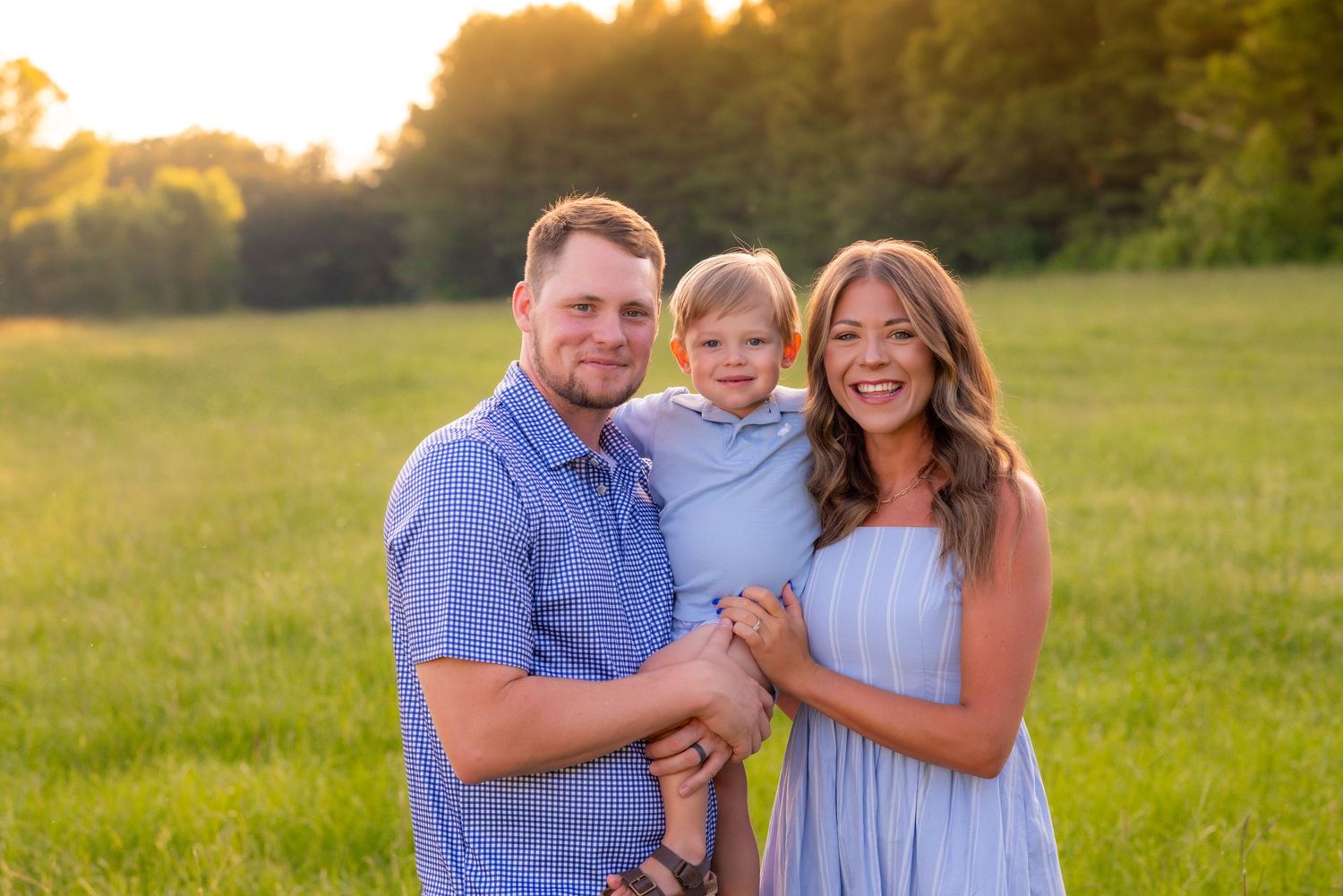 Young family with toddler son poses in golden sunset light in a lush green meadow for portraits.
