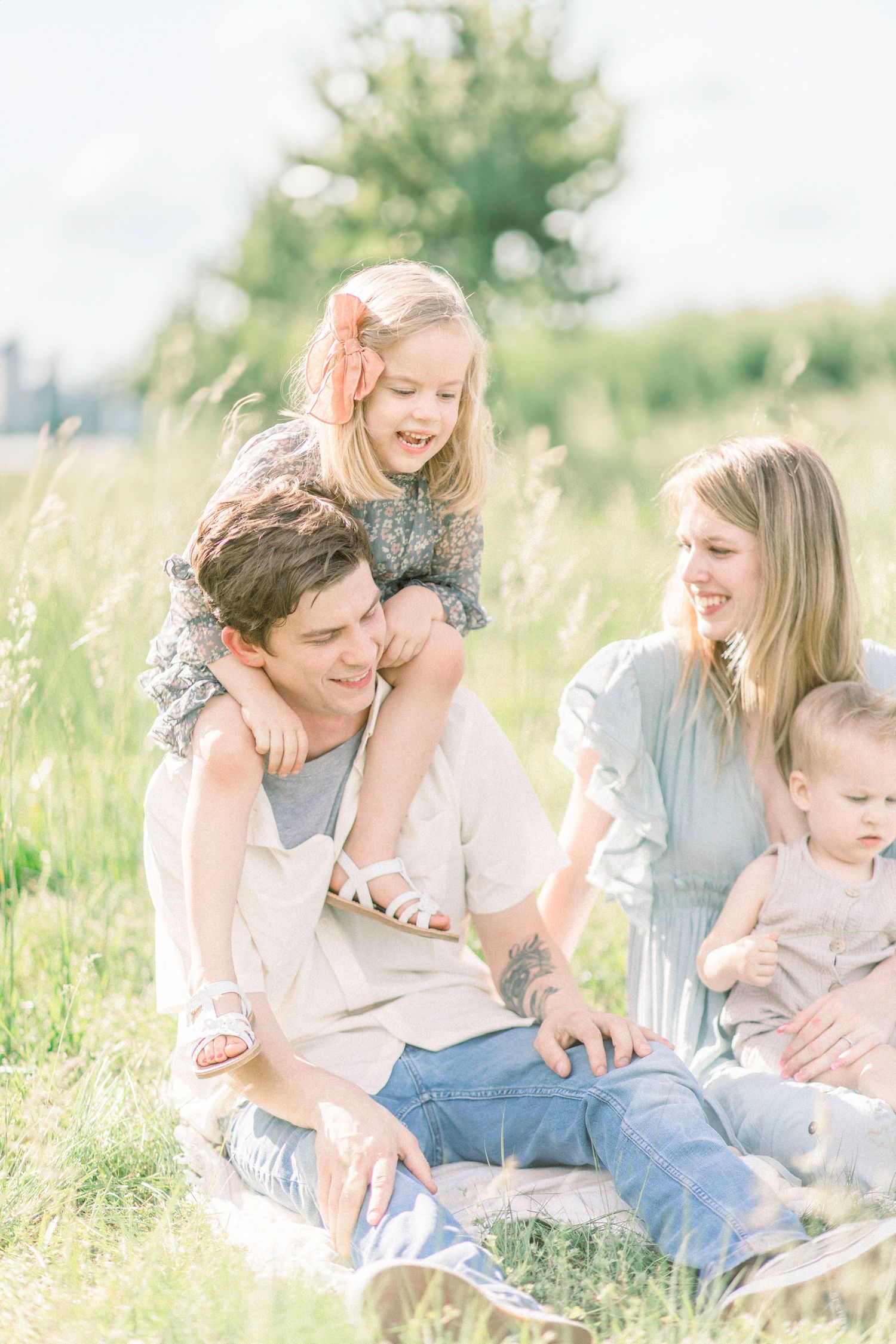 A joyful Springfield, Missouri family lounging together in a sun-drenched meadow of tall grass on a bright summer day.