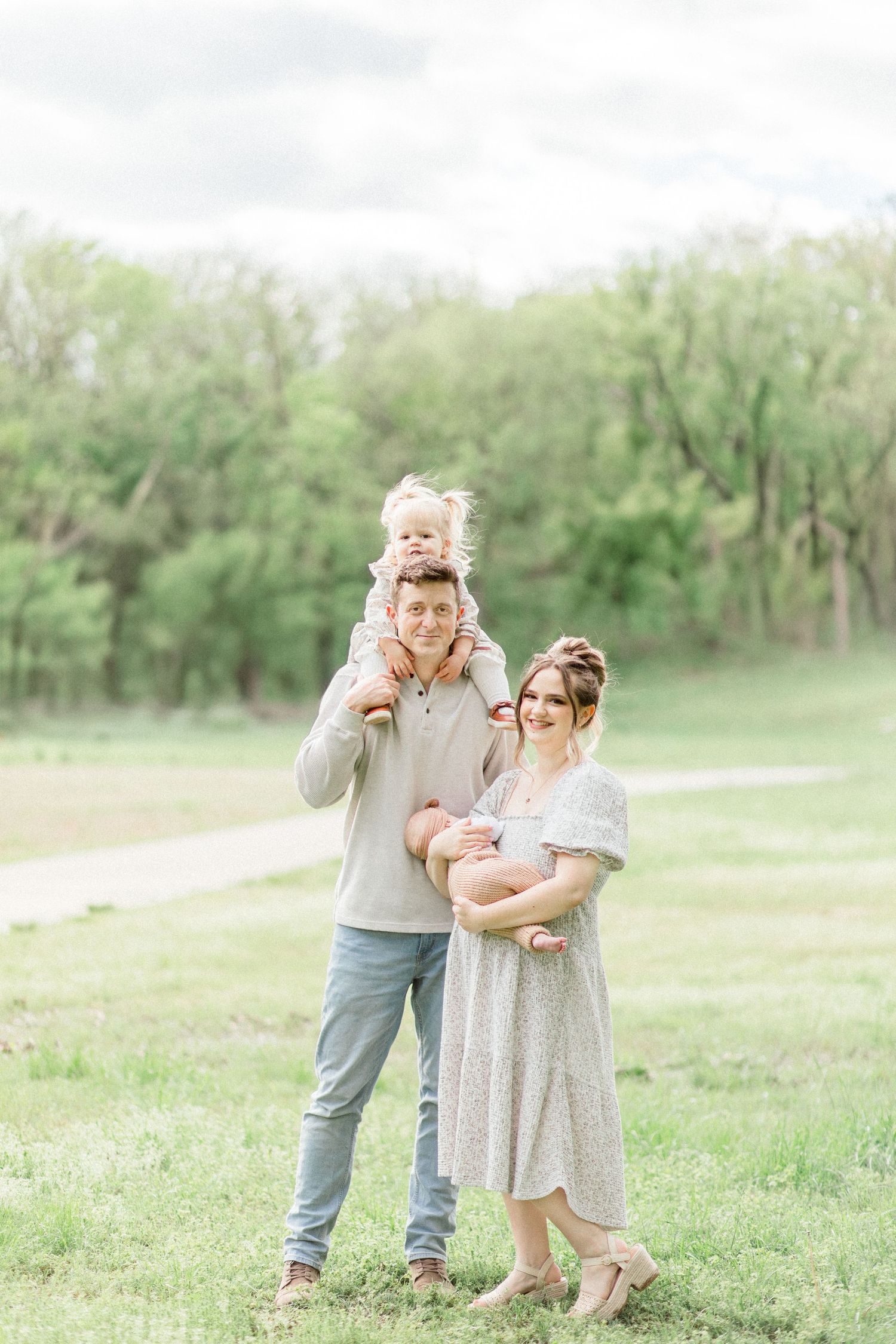 A Springfield, Missouri family stands together in a pasture setting with green trees and grass on a bright spring day.