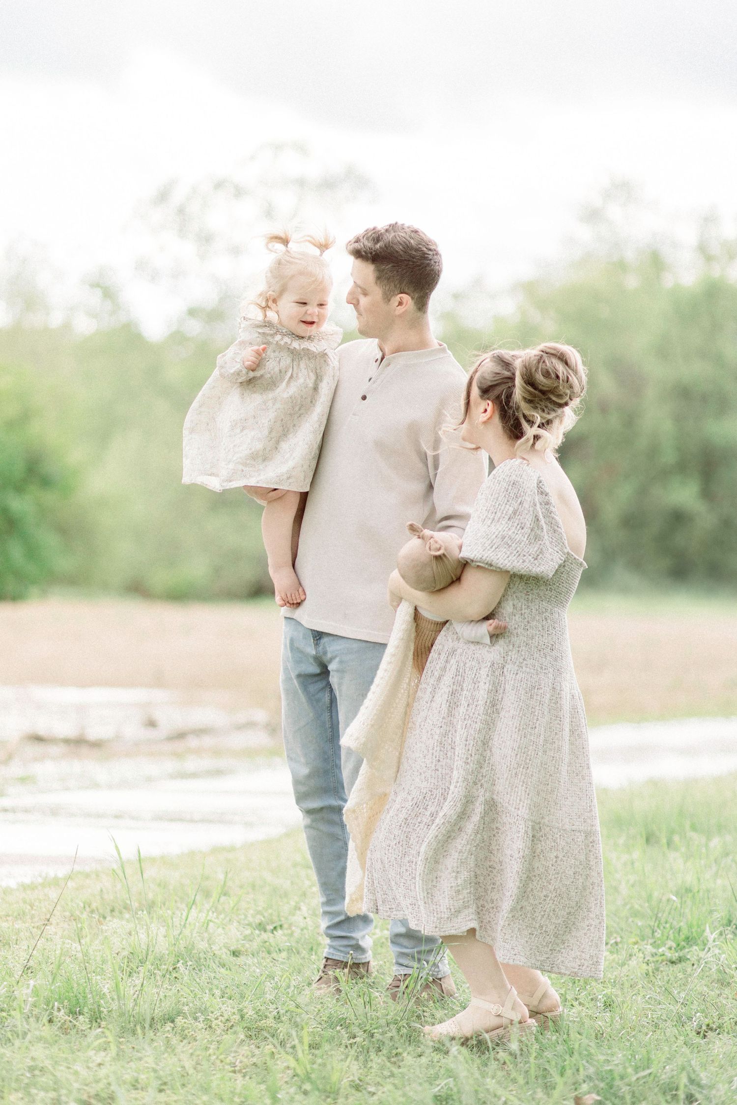 Family playing together in a sunlit field wearing coordinated neutral outfits.