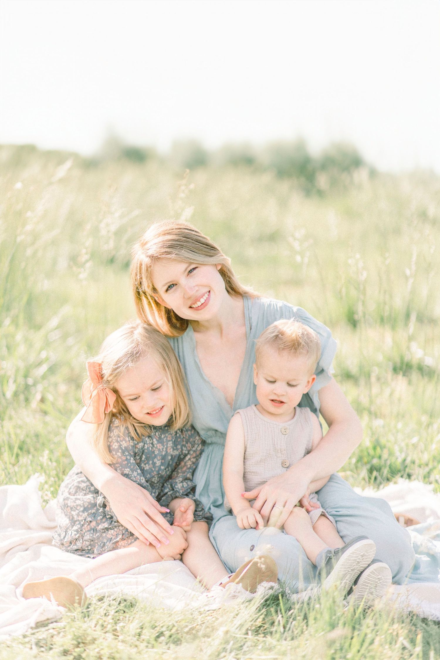 Mother sits with two children on a blanket in a sunny Fellows Lake meadow with tall grass in Springfield, Missouri.
