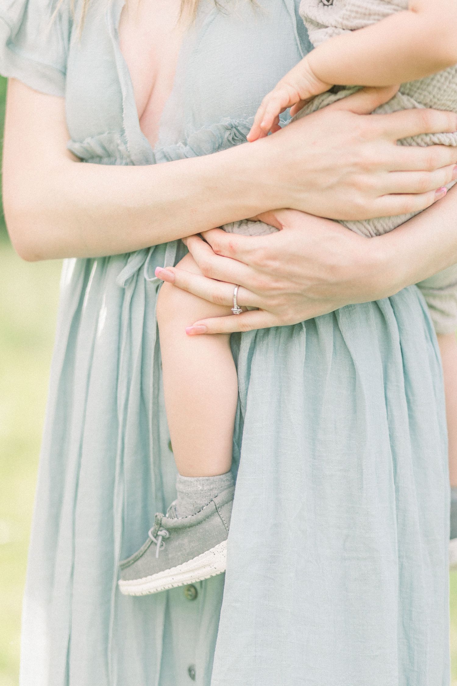 Close up of hands embracing while wearing a flowing light blue dress with an engagement ring visible in Springfield, Missouri family photos.