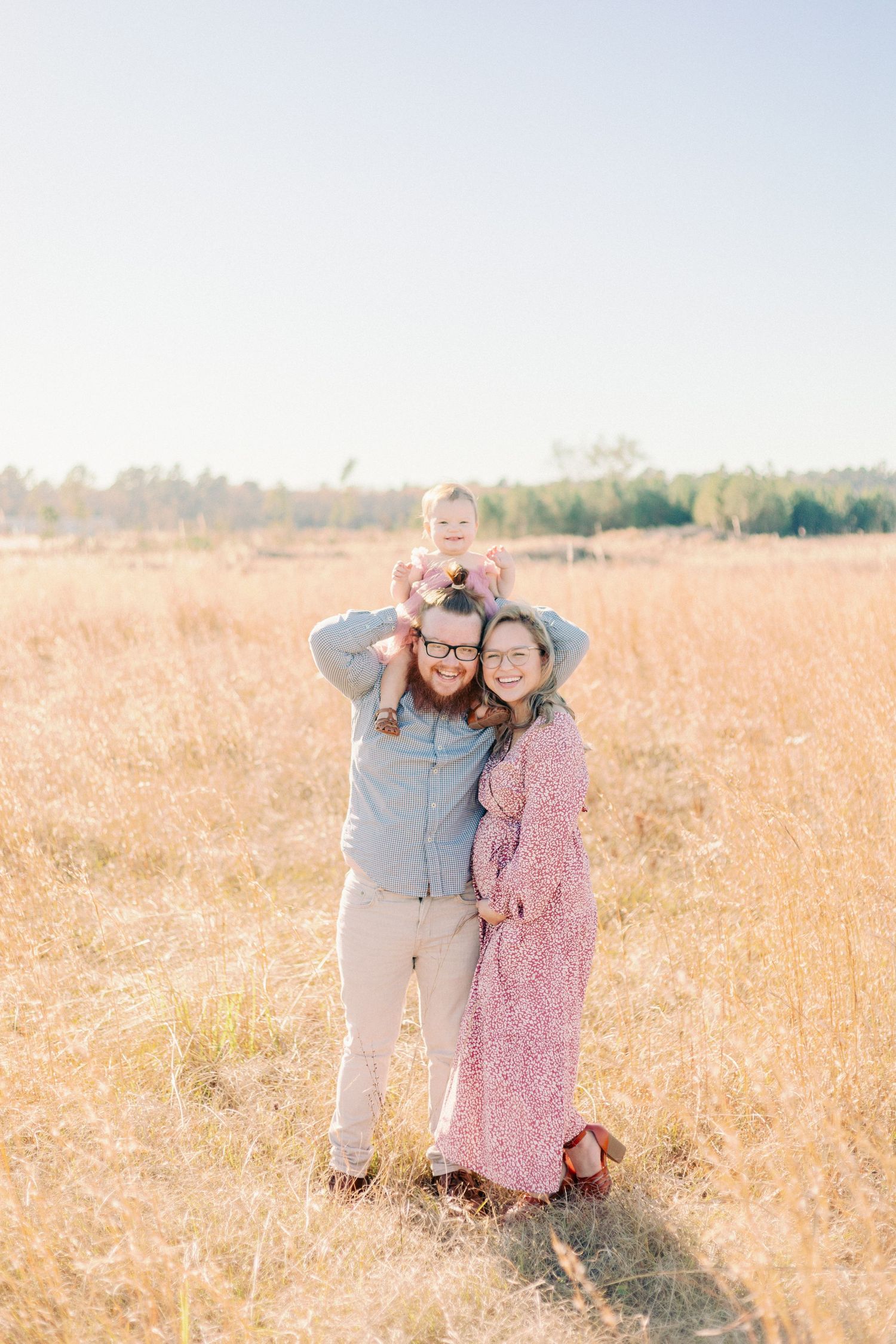 A family of three poses together in a sunlit golden field during autumn for Springfield Mo Photographer.