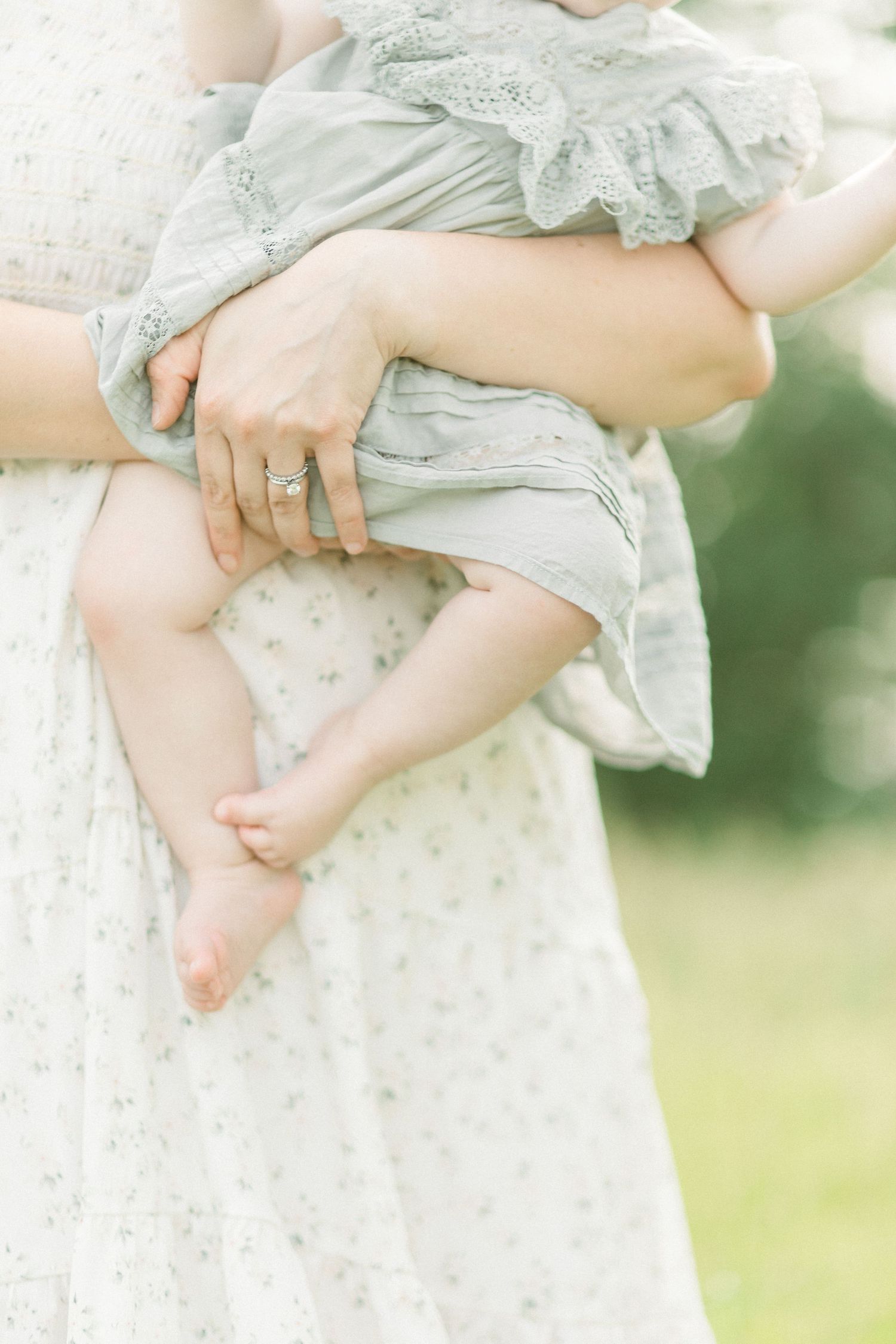 Close-up of tiny bare baby feet being held against a white lace dress in natural outdoor lighting in Springfield, MO.