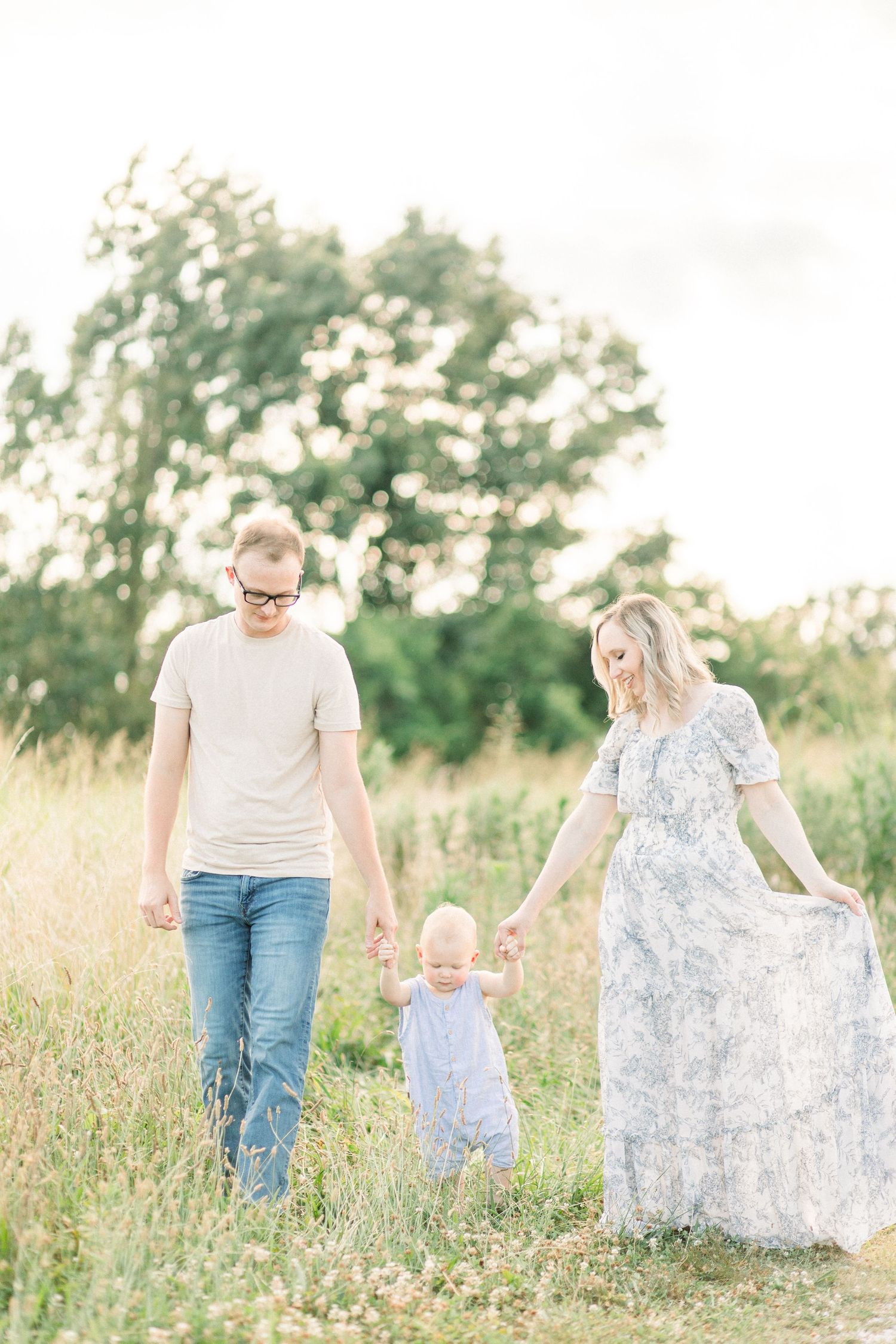 Family walking together through a sunlit meadow with tall grass and wildflowers during golden hour in Springfield, MO's Fellows Lake.