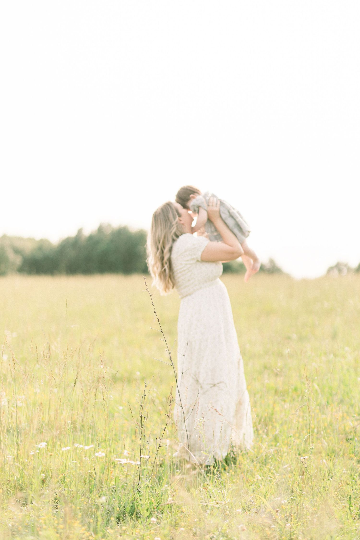 A person in a flowing white dress stands gracefully in a sunlit meadow filled with wildflowers and tall grass in Marshfield, Missouri.