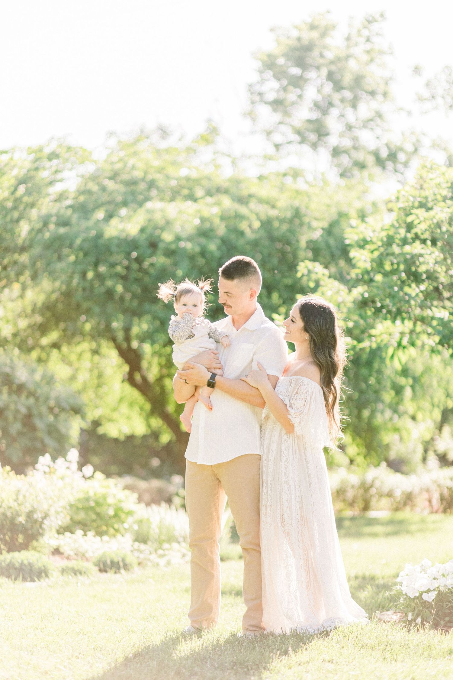 A family in white outfits embraces together in a sun-drenched garden setting during a golden hour photoshoot in Springfield, Missouri.