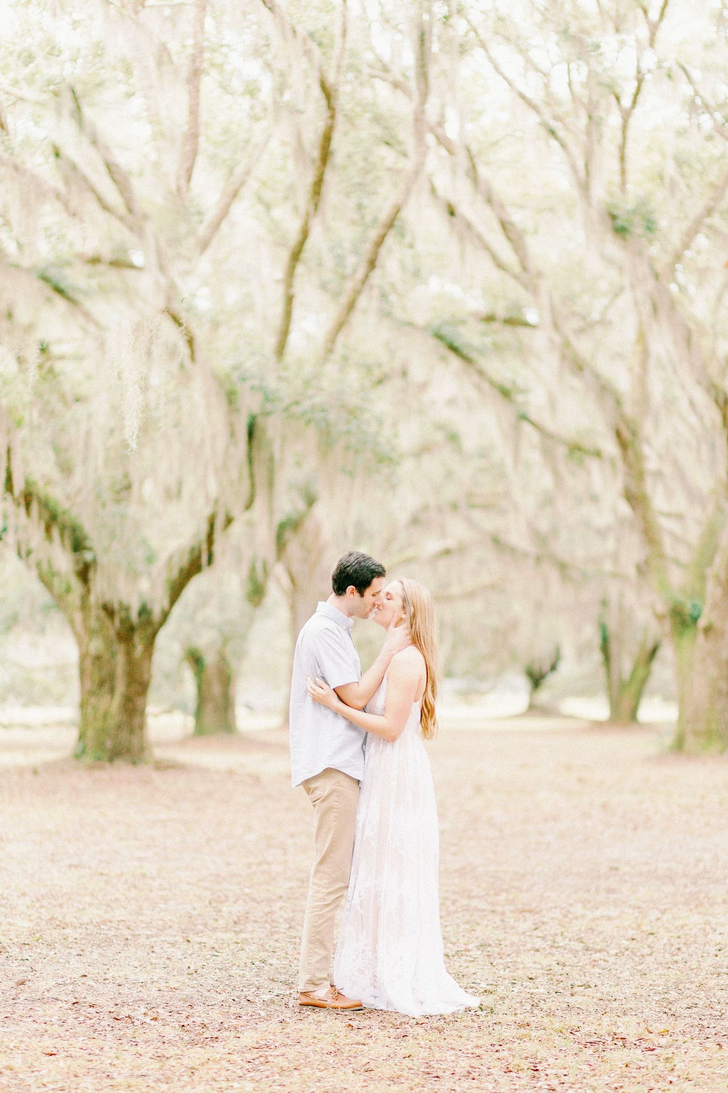 A romantic couples session by a Springfield, MO photographer. A couple shares a kiss beneath Spanish moss trees.