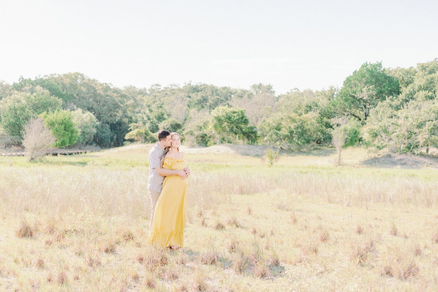 A person in a flowing yellow dress walks through a sunny meadow with tall grass and wildflowers.