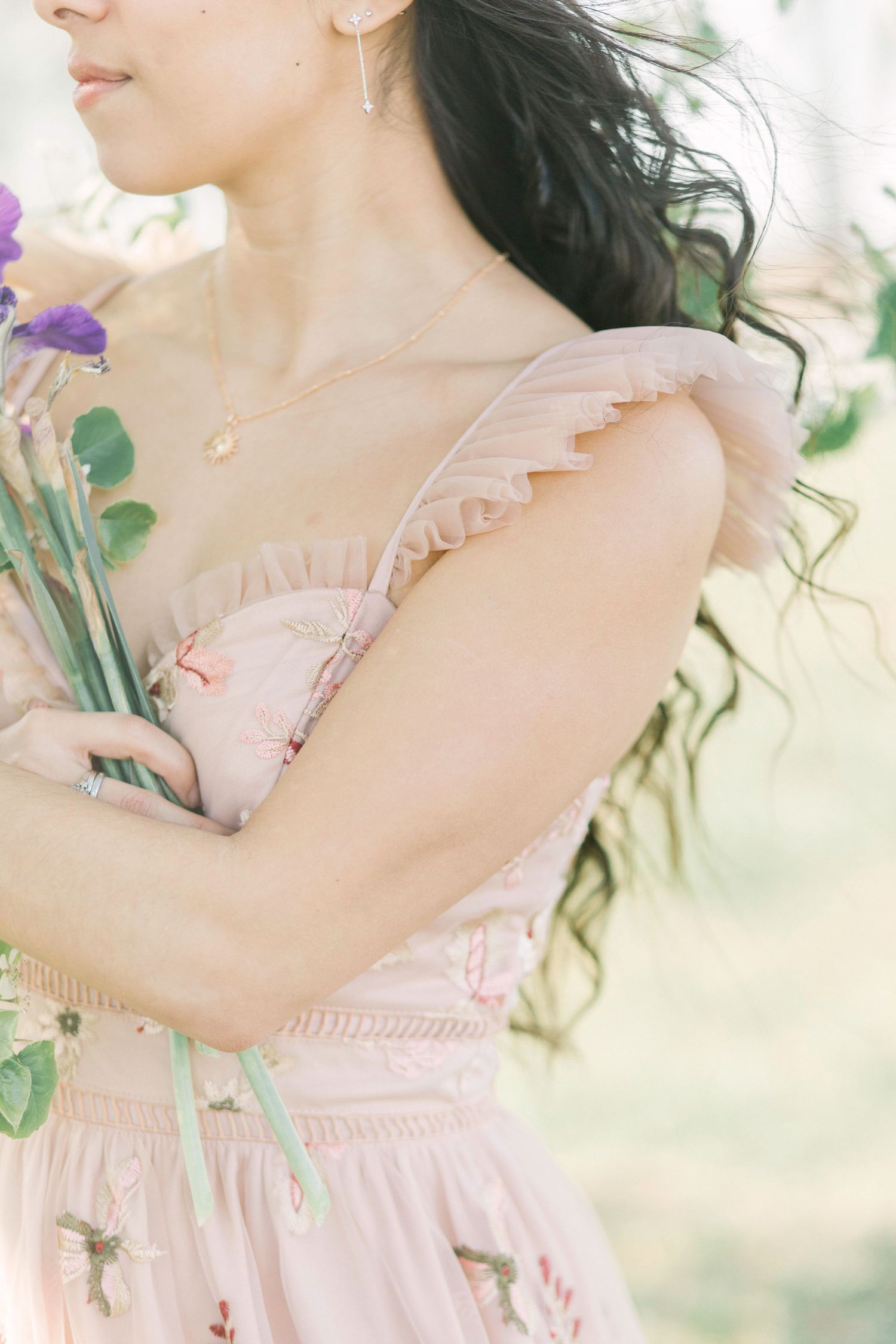 A dreamy portrait of someone in a pink ruffled dress holding purple flowers with soft sunlit ethereal lighting in Springfield, Missouri.