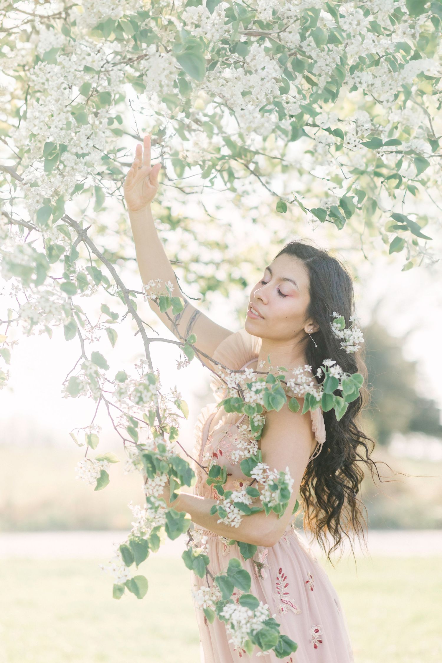Ethereal spring portrait showing a dreamy scene with white blossoms, soft lighting, and a pink dress in a garden setting in Springfield, MO.