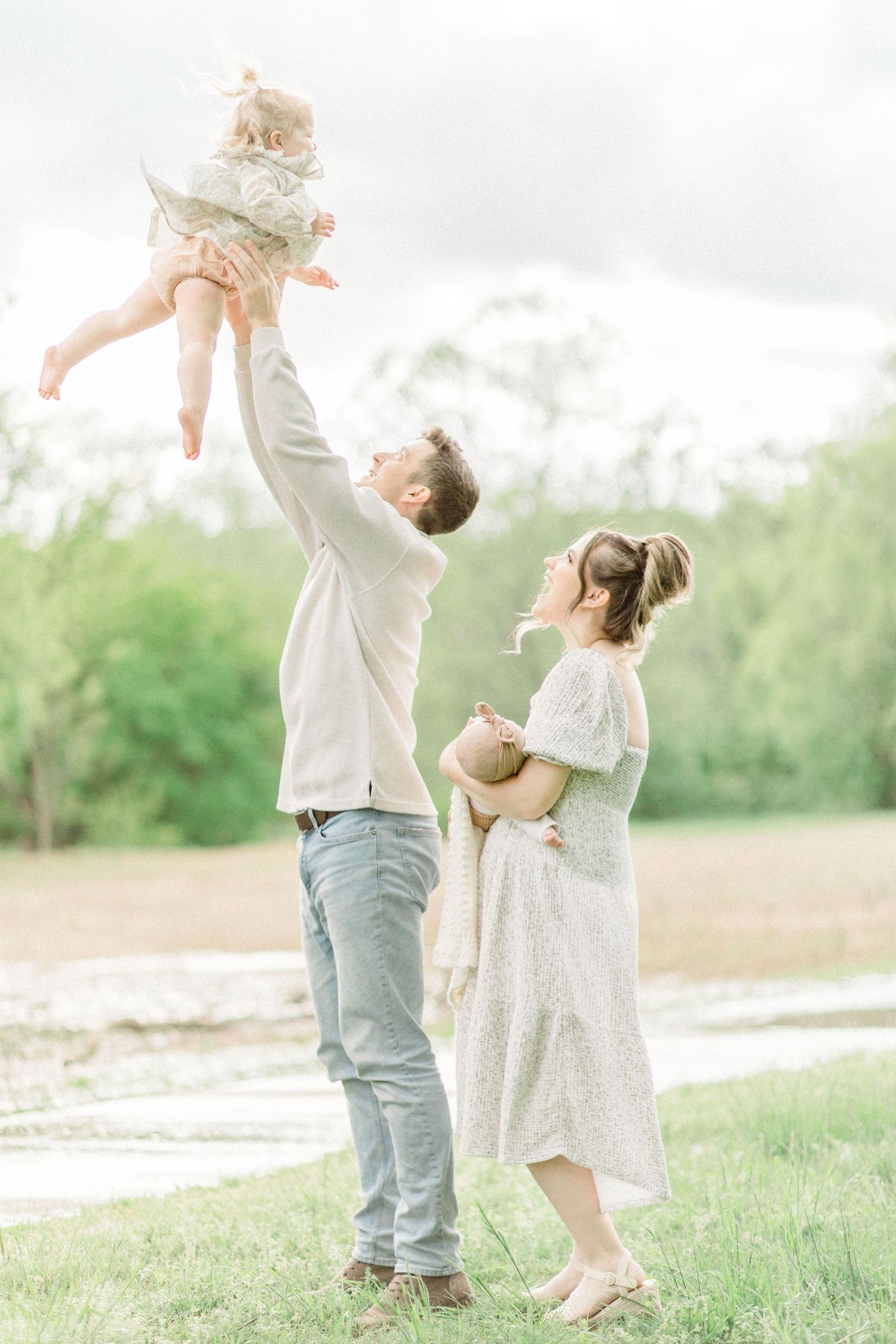 Family of three enjoying a playful moment together in a Springfield, Missouri sunlit field with soft dreamy lighting.