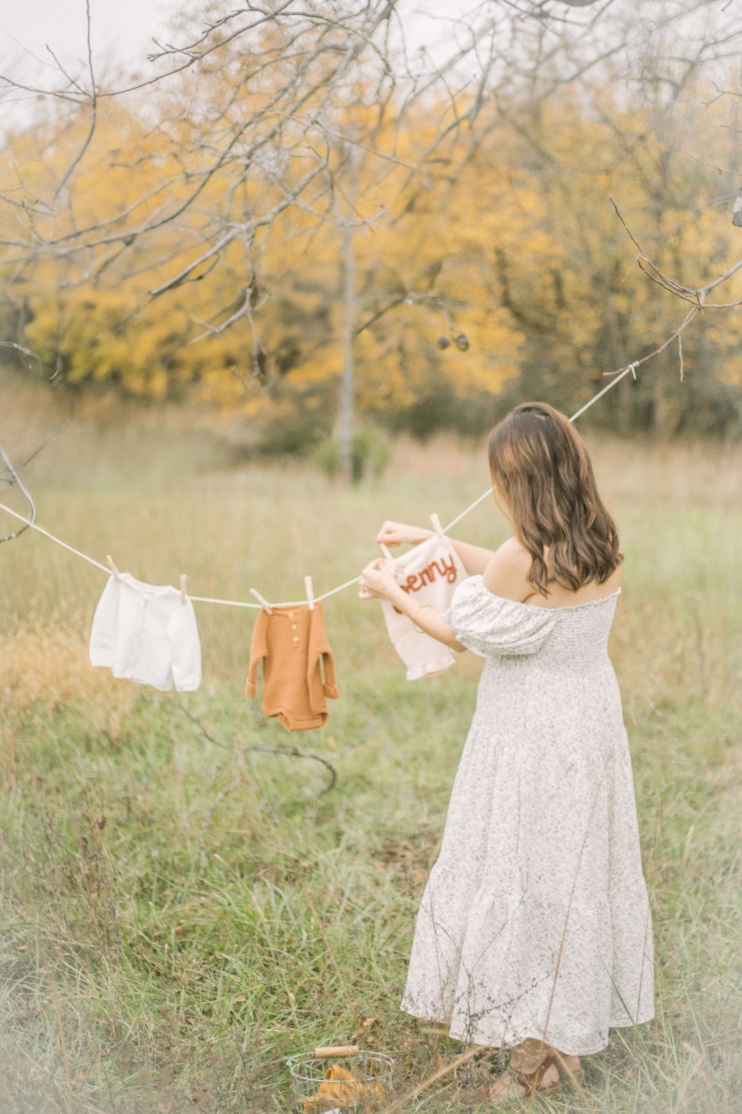 Whimsical baby clothes hanging on clothesline in autumn field with golden trees in Springfield, MO.