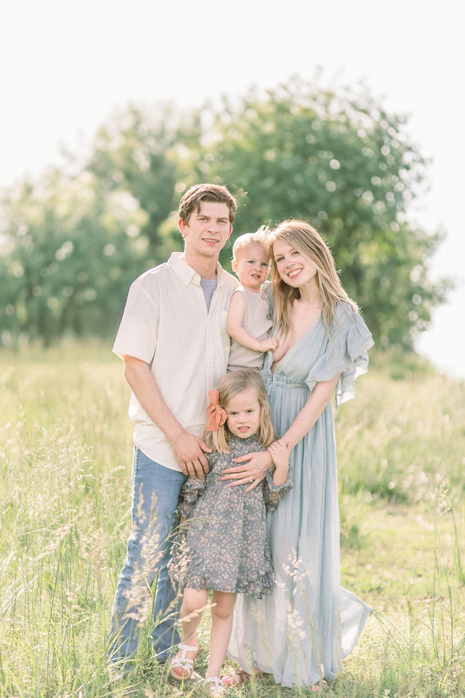 A family stands together in a sunny meadow wearing coordinated light blue and white outfits on a warm summer day in Springfield, Missouri.