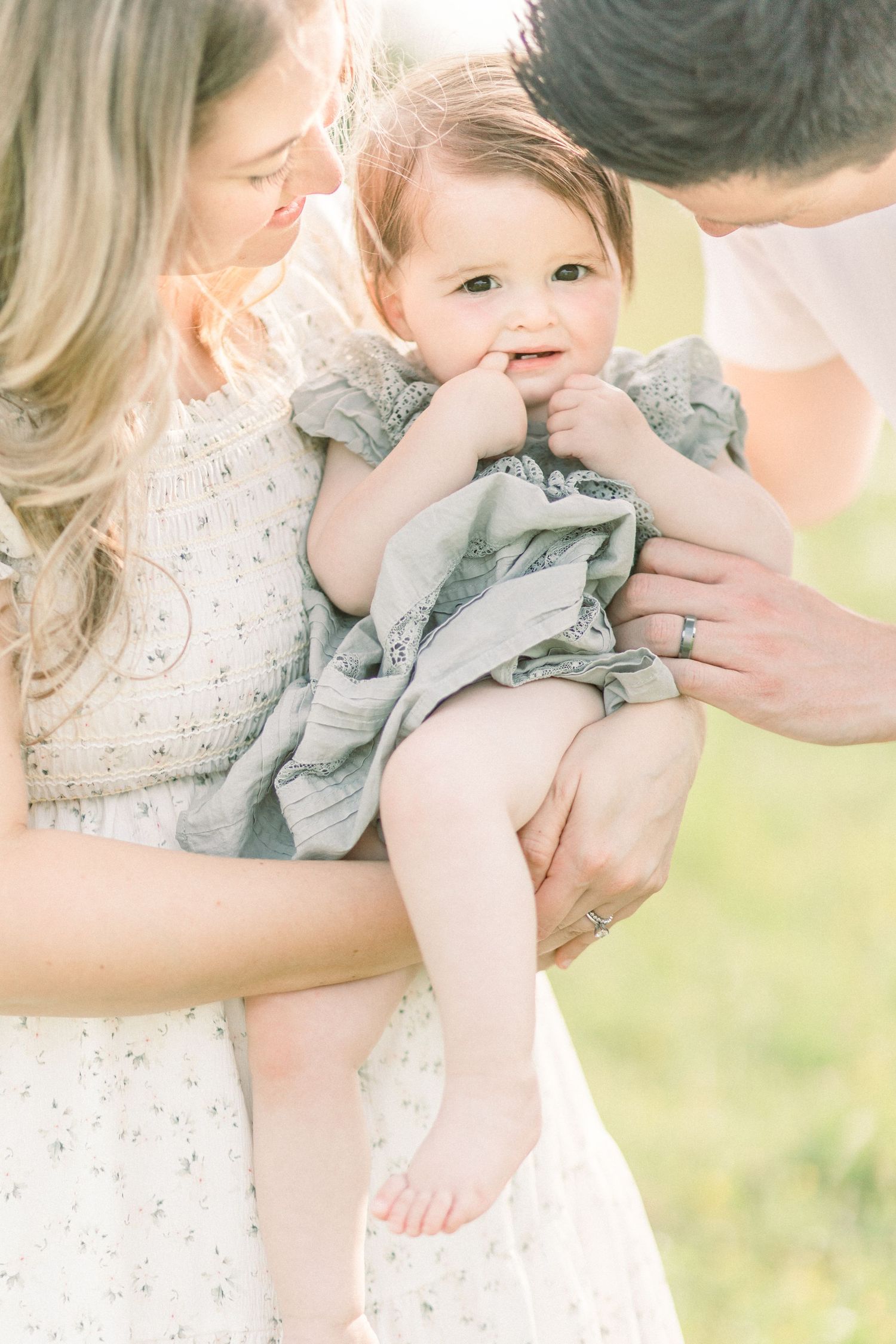 A tender family moment captured in soft light showing parents cuddling with their baby in a white dress in Marshfield, MO.