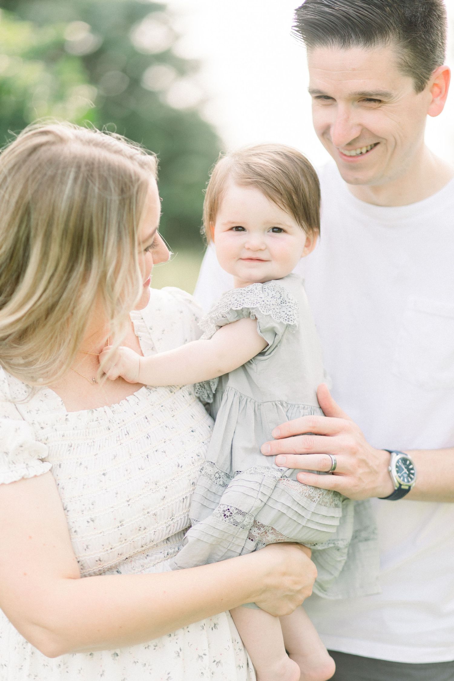 Family portrait series showing sweet interactions between parents and their small child in matching light outfits in Springfield, Missouri.