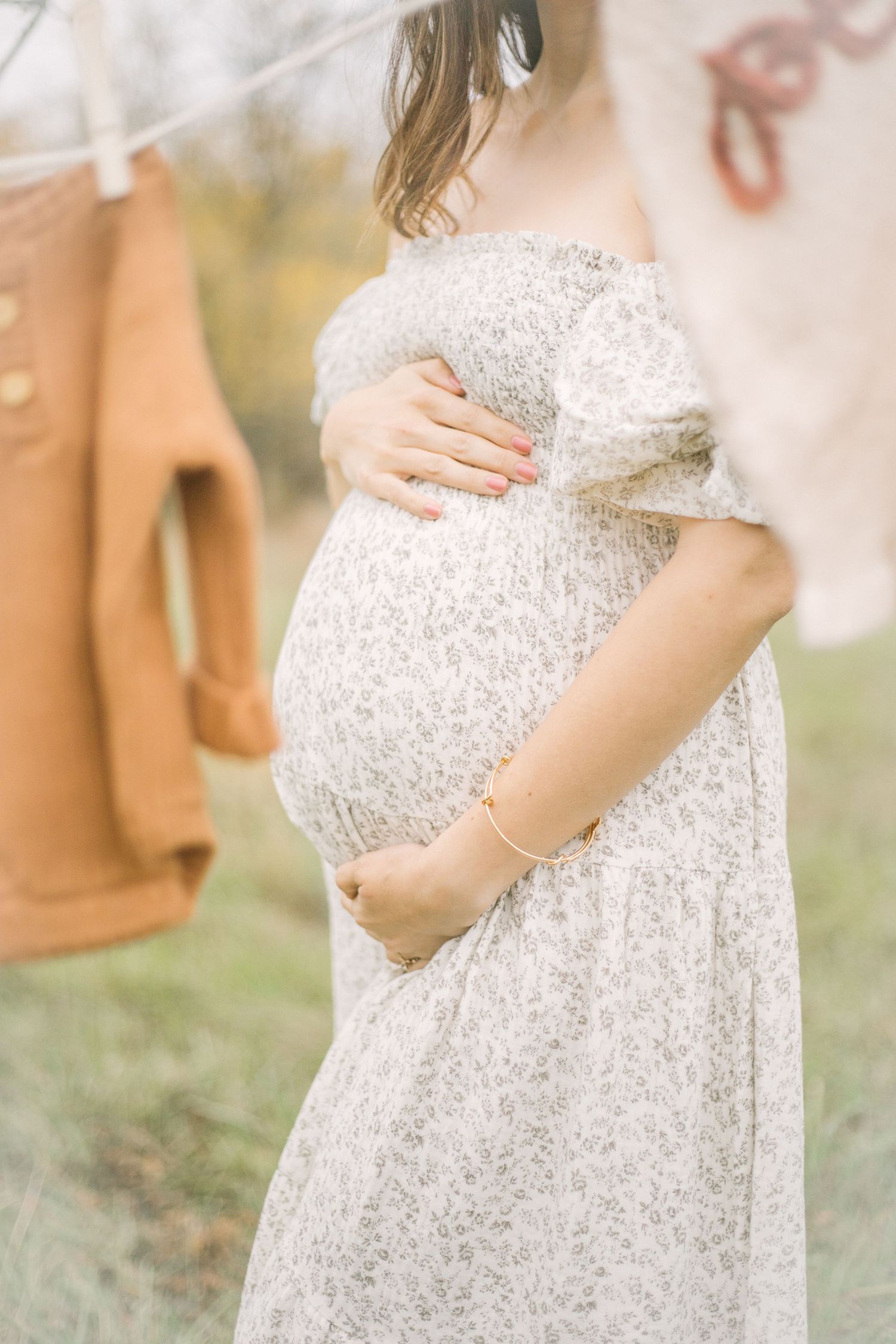 A pregnant woman in a delicate white floral dress cradles her baby bump while standing in Springfield, MO.