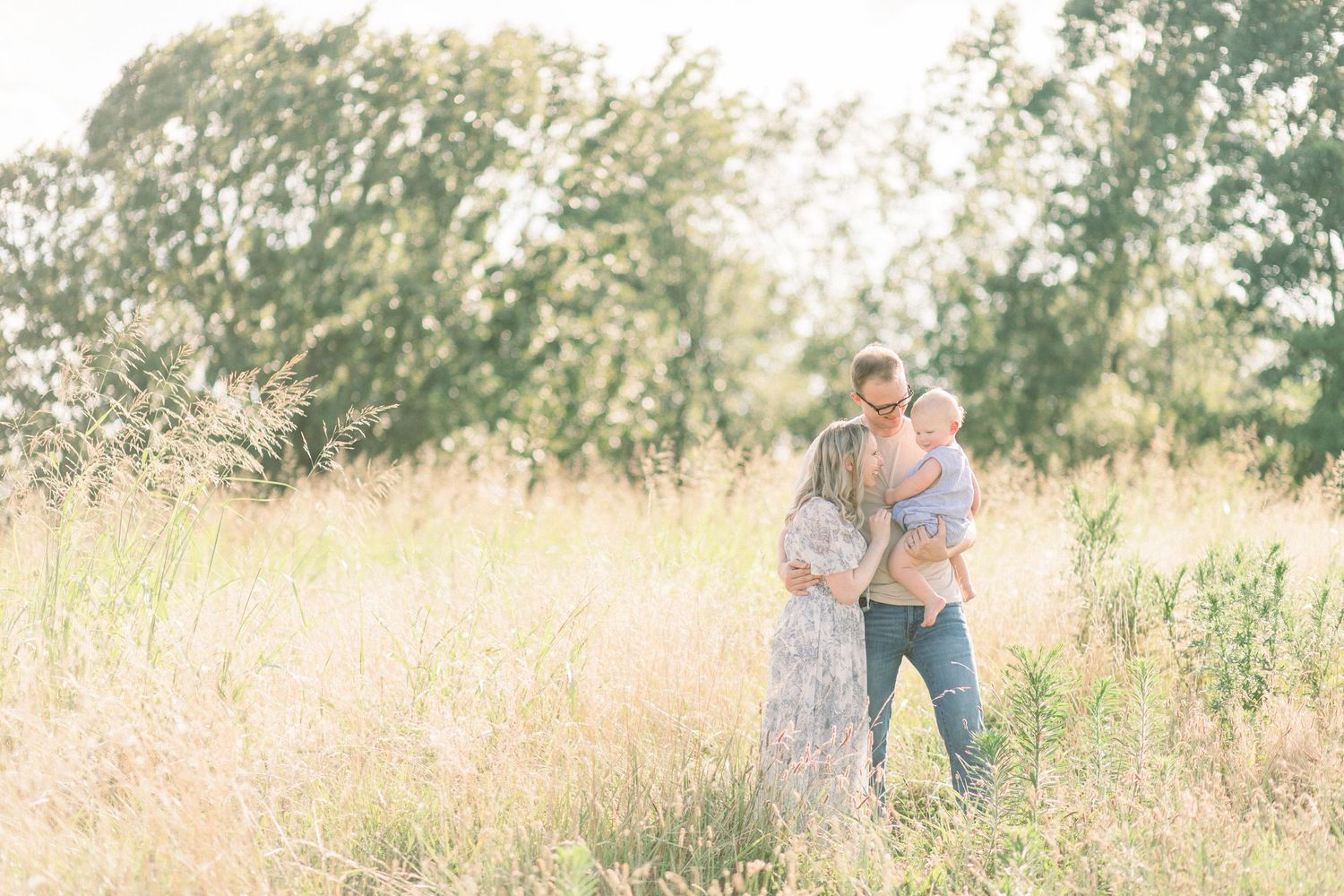 A family embraces in a sun-drenched field with golden grass and trees during a sweet Springfield, MO photo session.