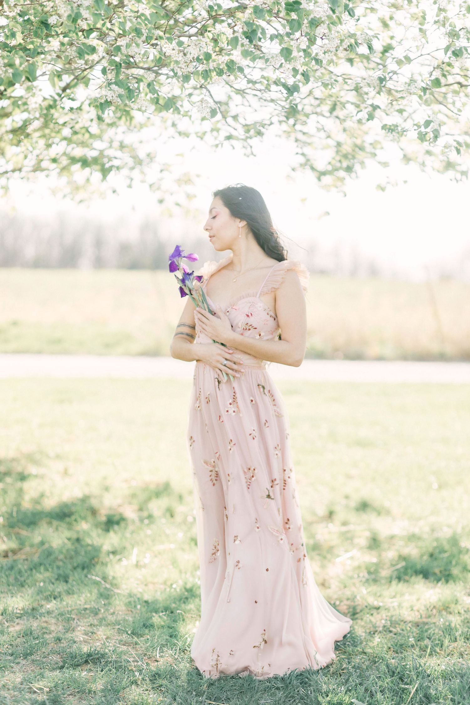 A romantic spring scene with a flowing pink floral gown and purple bouquet against blooming trees and sunlit meadow in Springfield, Missouri