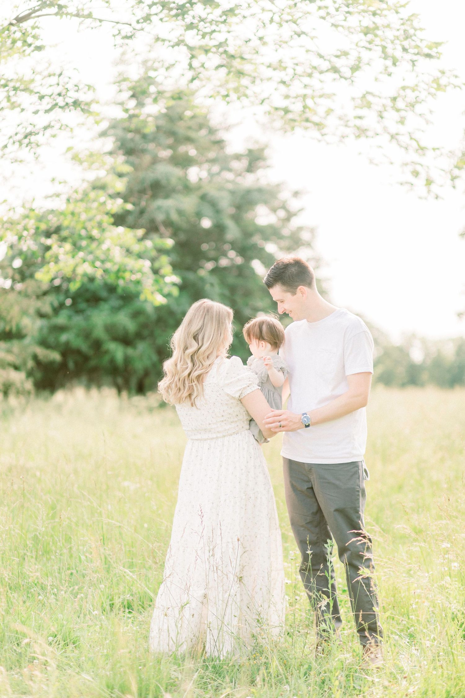 A family shares tender moments together in a sunlit meadow with tall grass and soft natural lighting in Marshfield, MO.