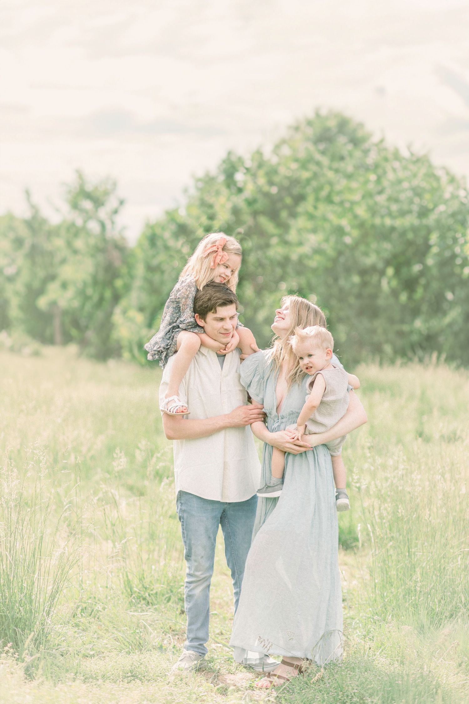 Family enjoying a tender moment together in a sunlit meadow with green trees in the background in Springfield, Missouri.