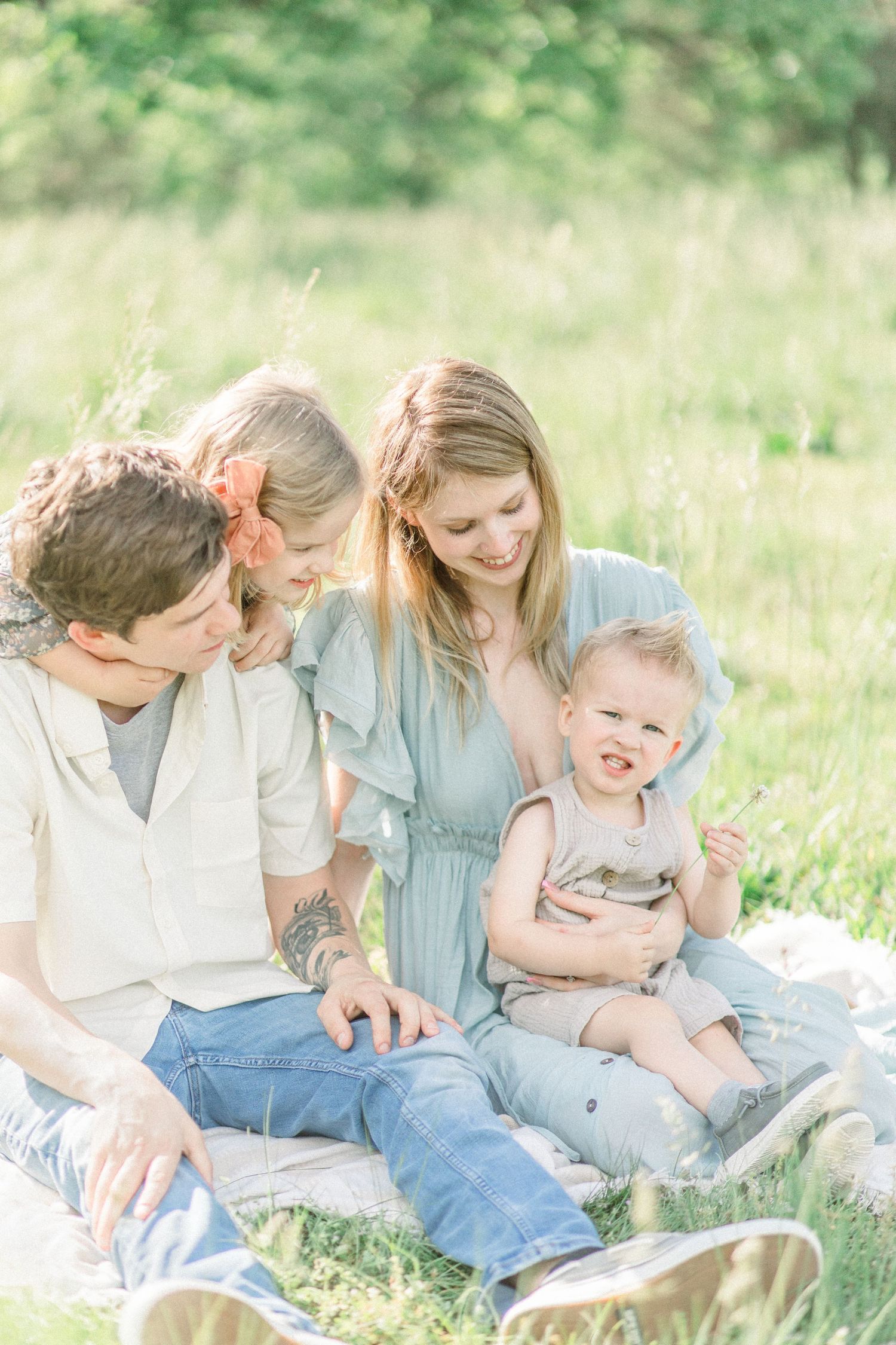 A family sits together on a blanket in a sunlit meadow with tall grass on a bright summer day at Fellows Lake in Springfield, Missouri.