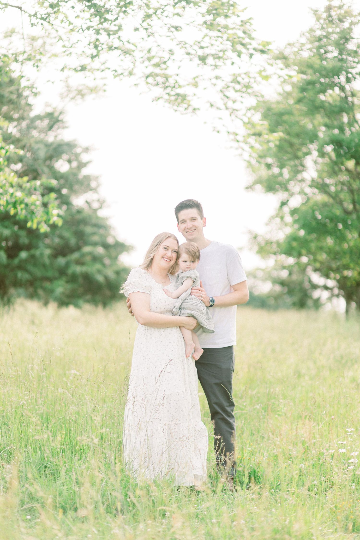 Family embracing in sunny meadow with green trees and tall grass in Marshfield, Missouri.