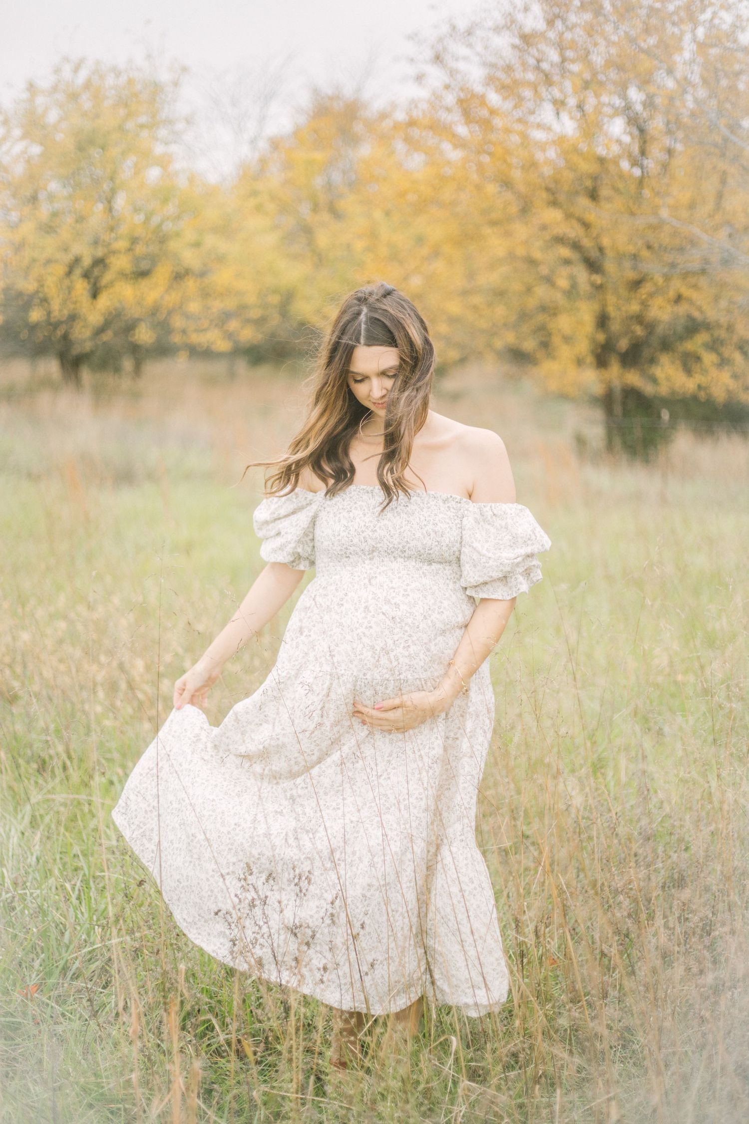 A dreamy series of maternity photos showing a mama in a white dress twirling in a sunlit autumn field with golden grass in Springfield, MO.