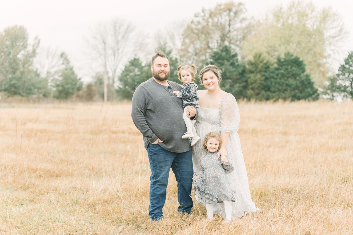 A family poses together in a golden autumn field with evergreen trees in the background in Springfield, Missouri.