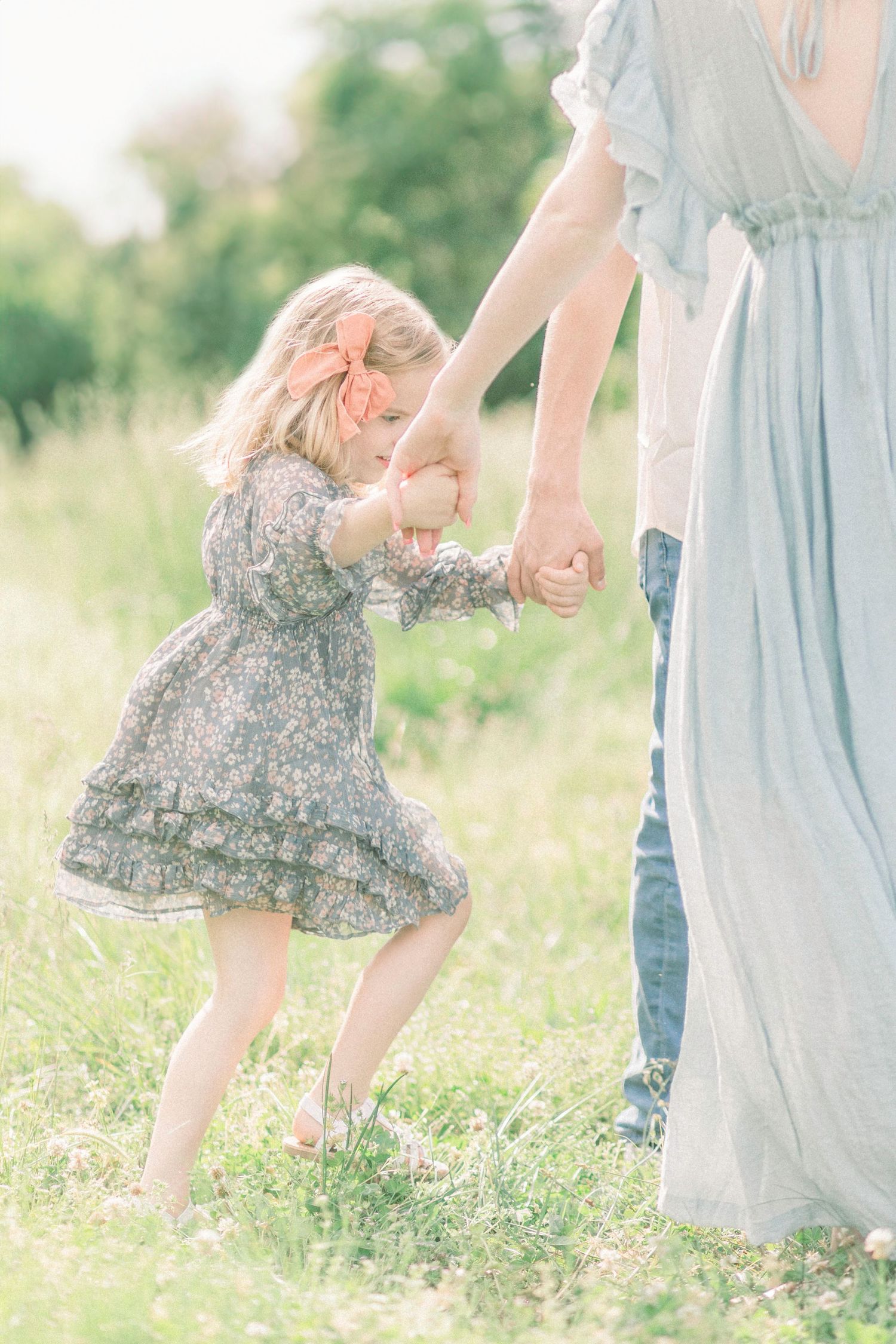 A child in a floral dress dances and holds hands with adults in a sunlit Fellows Lake field in Springfield, Missouri.