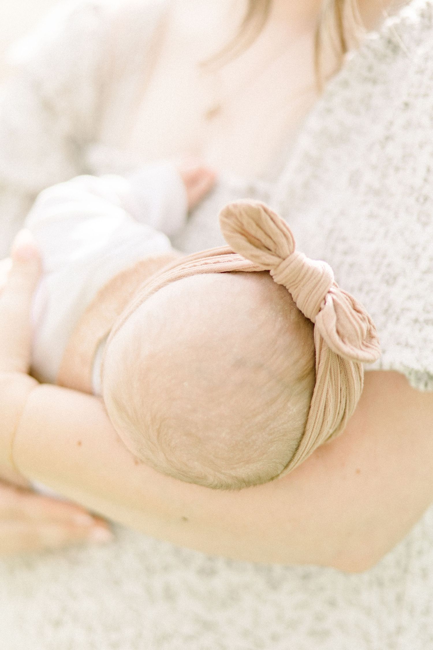 Close up of a sleeping baby's head with a soft blush colored bow on top in a dreamy light setting in Springfield, Missouri.
