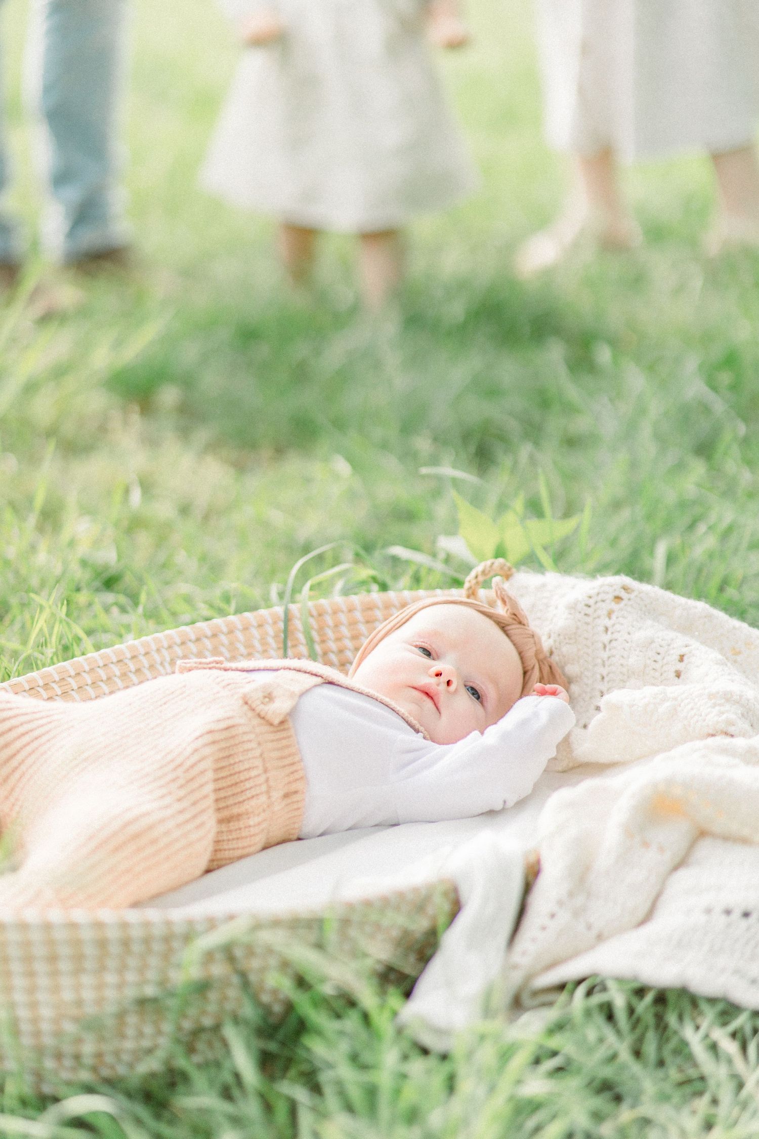 Baby resting on picnic blanket outdoors in soft peach clothing while lying on grass in Springfield, Missouri.