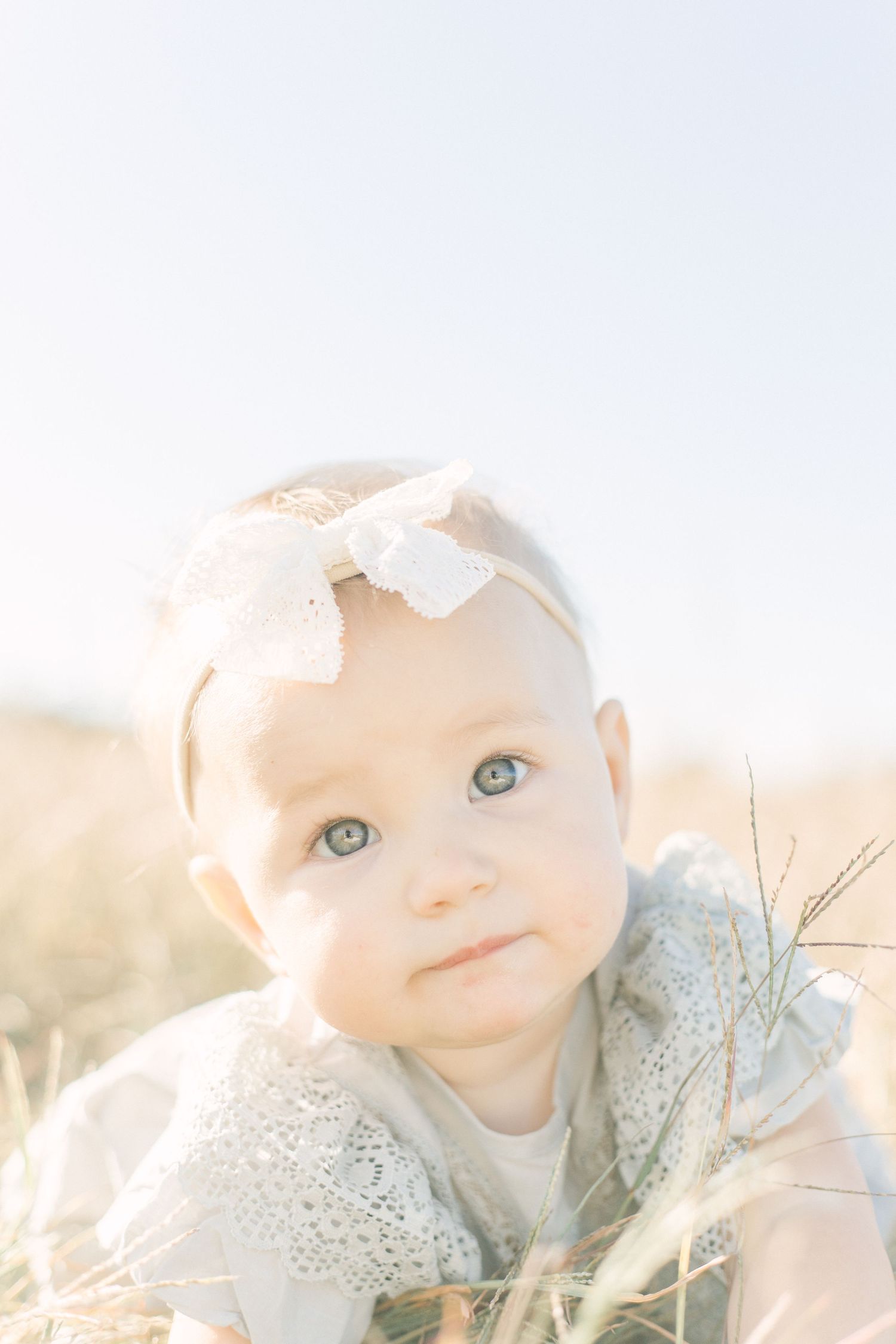A dreamy closeup portrait of a baby wearing a white bow headband in golden sunlight in Springfield, MO.