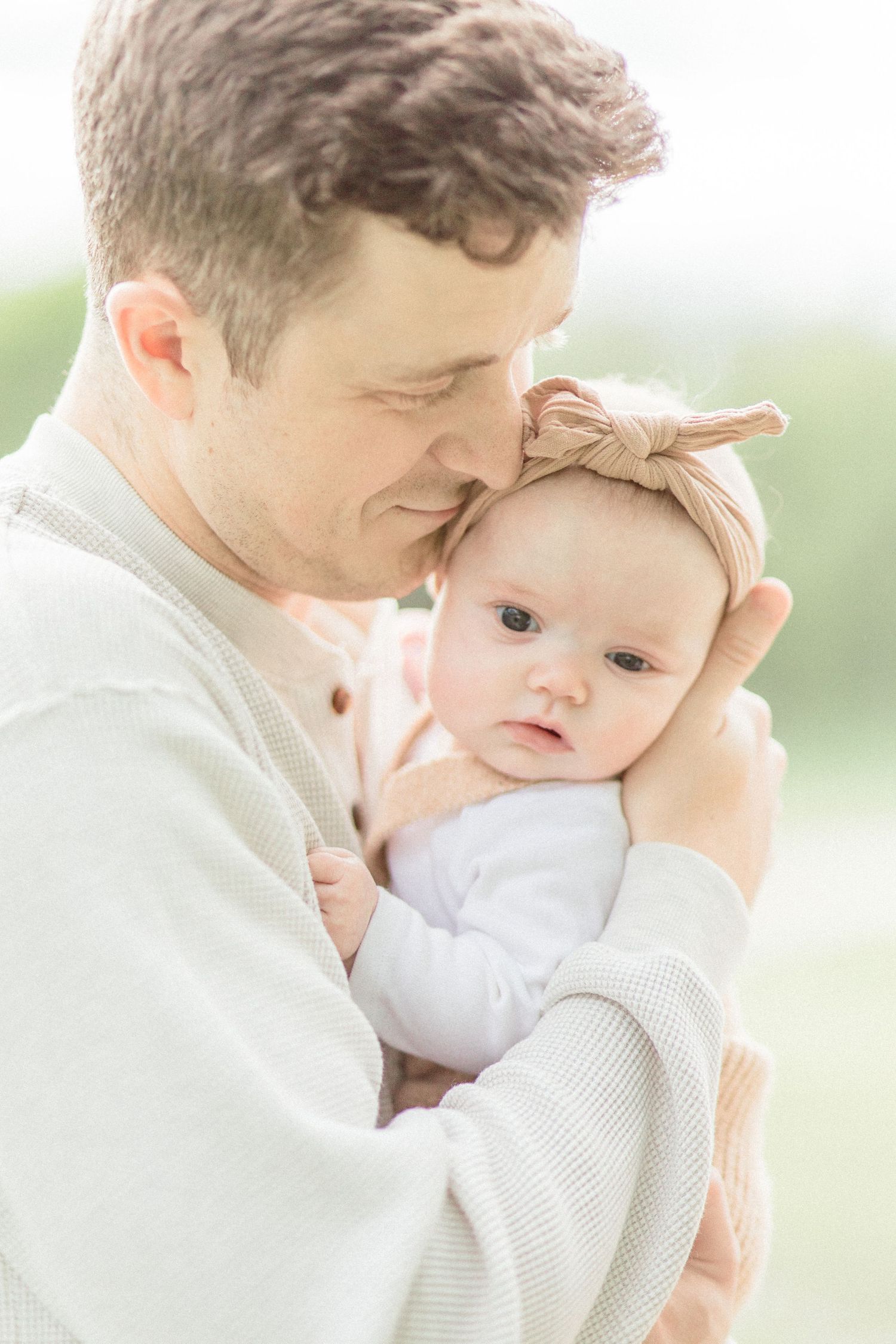 A tender moment shows a Springfield, Missouri dad in a cream sweater cradling a baby wearing a bow headband.