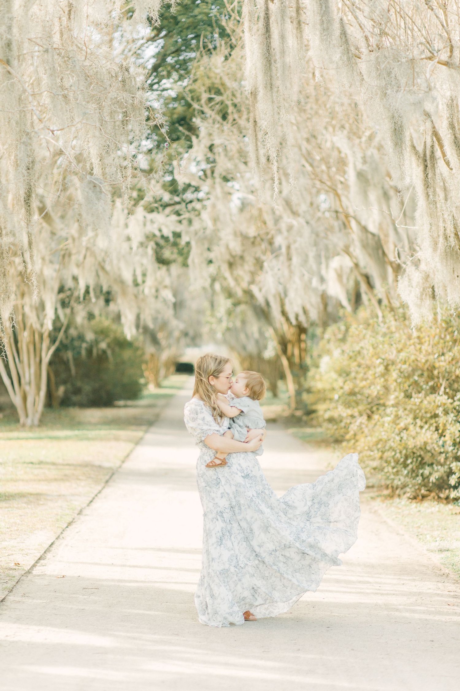 A flowing white lace dress swirls beneath Spanish moss in a romantic garden pathway in Charleston, South Carolina.